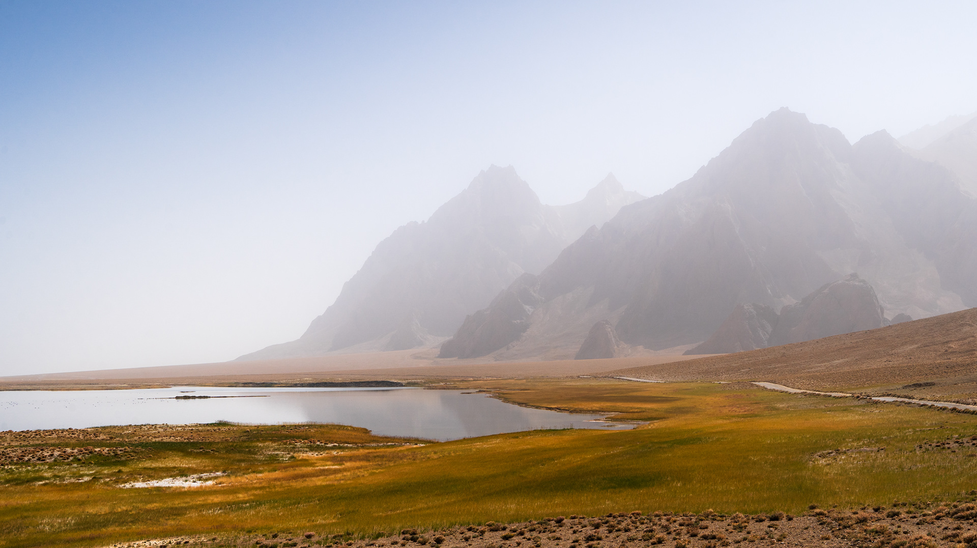Hazy peaks rise above Rangkul lake and the colourful vegetation around it, Pamir, Tajikistan