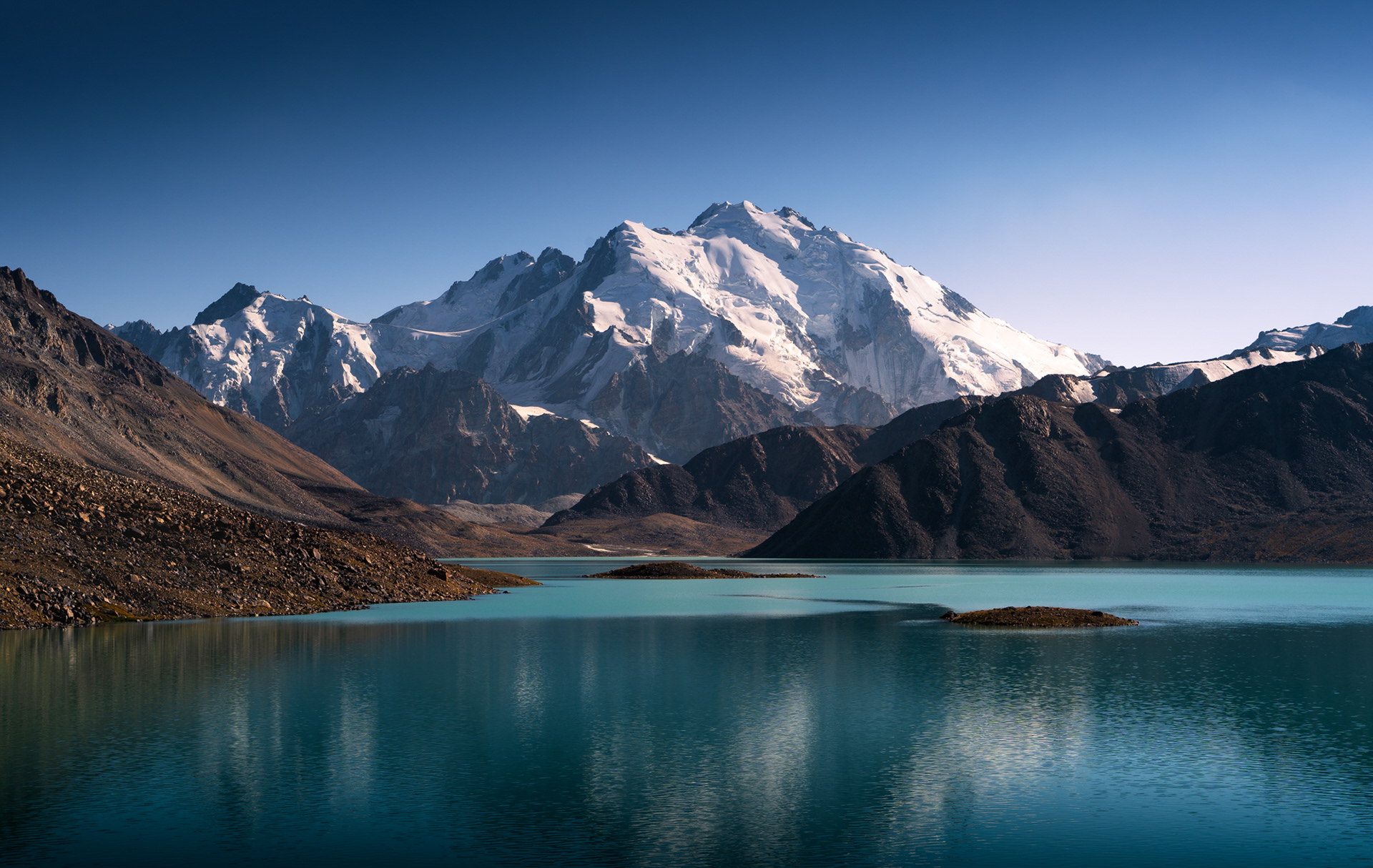 A large glaciated mountain rises above the emerald Zaroshkul Lake.