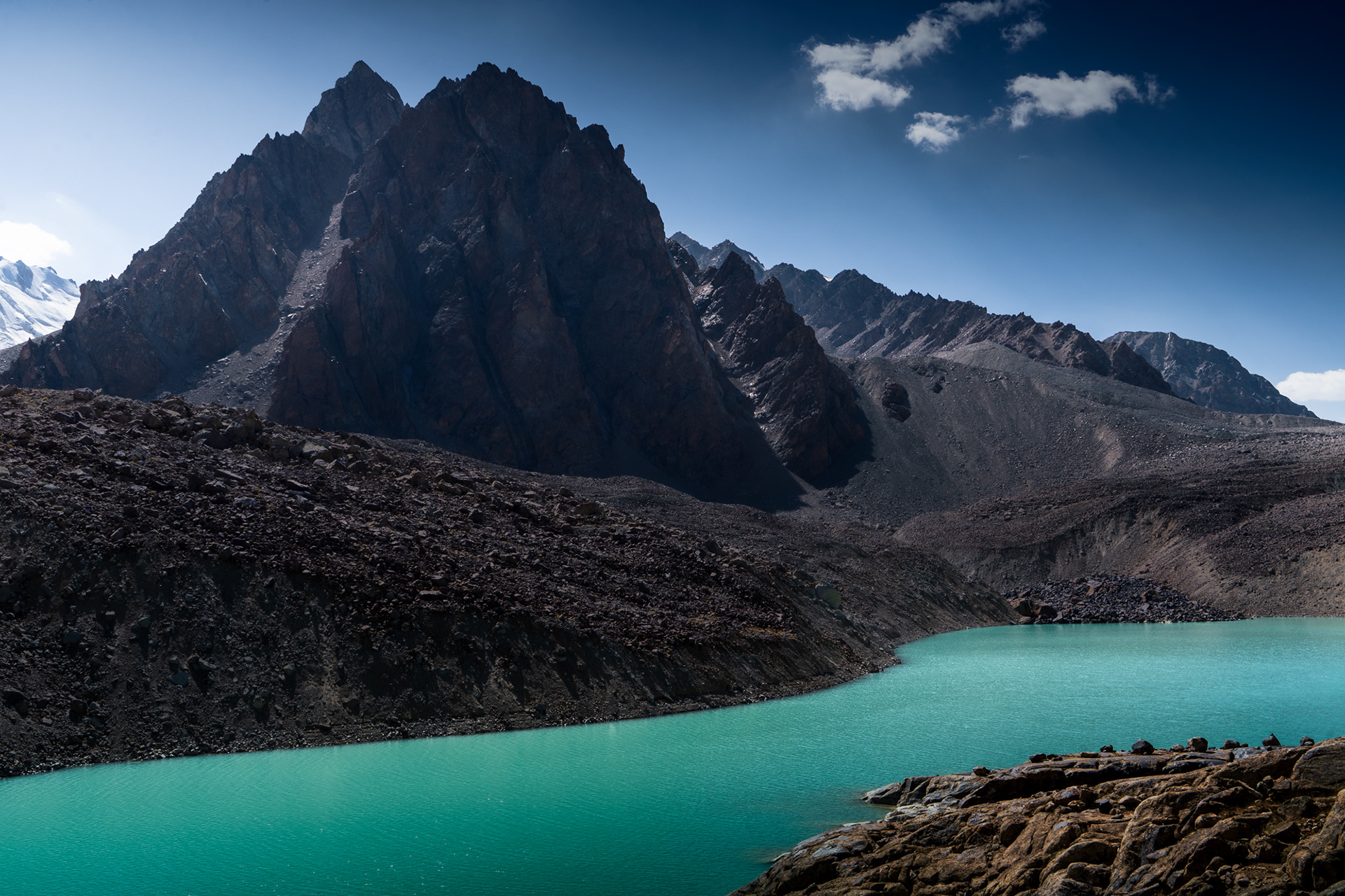 A jagged peak rises above a calm Tsaxinkul Lake in Tajikistan Pamir Mountains.