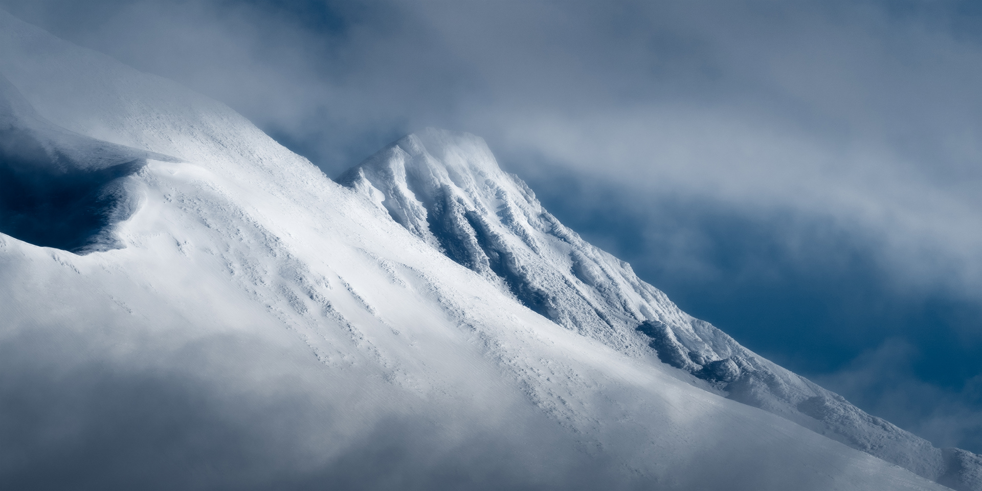A zoom photo of the Ahkka Massif in Stora Sjofallet National Park, Swedish Arctic. The peaks are covered in snow and glaciers, and dramatic light emerges from the clouds