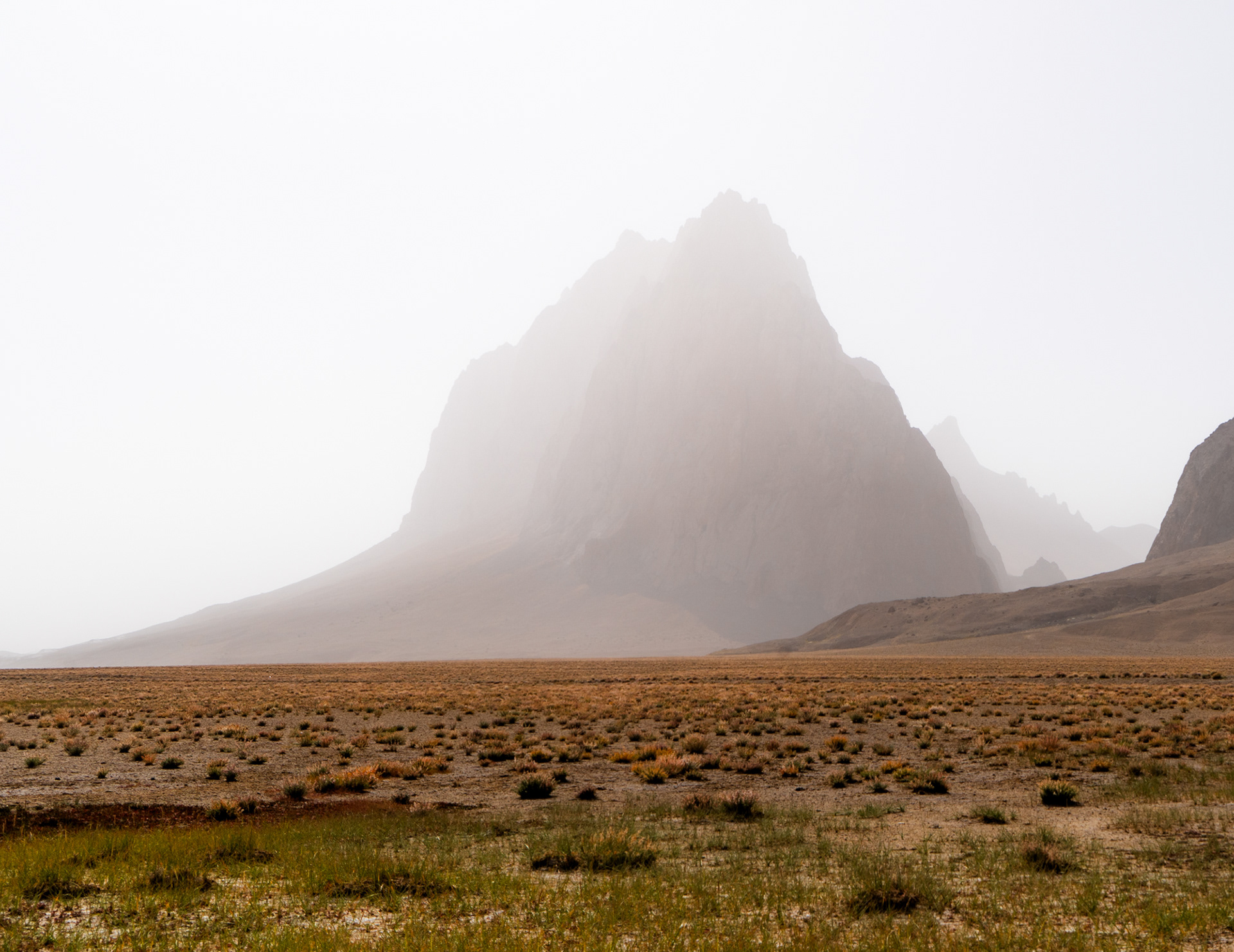 Rugged peaks rise from the haze above the colourful grasses of Rangkul, Pamir, Tajikistan