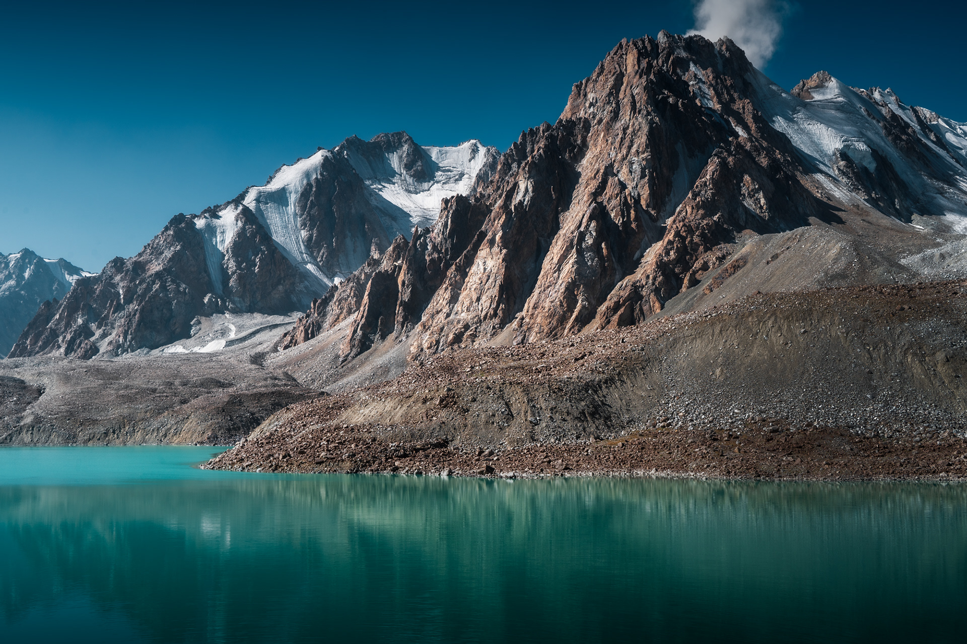 Jagged peaks of the Shakhdara Range rise above Tsaxinkul Lake, a glacial lake at 4300m deep in the Tajik National Park of the Pamir Mountains, Tajikistan.