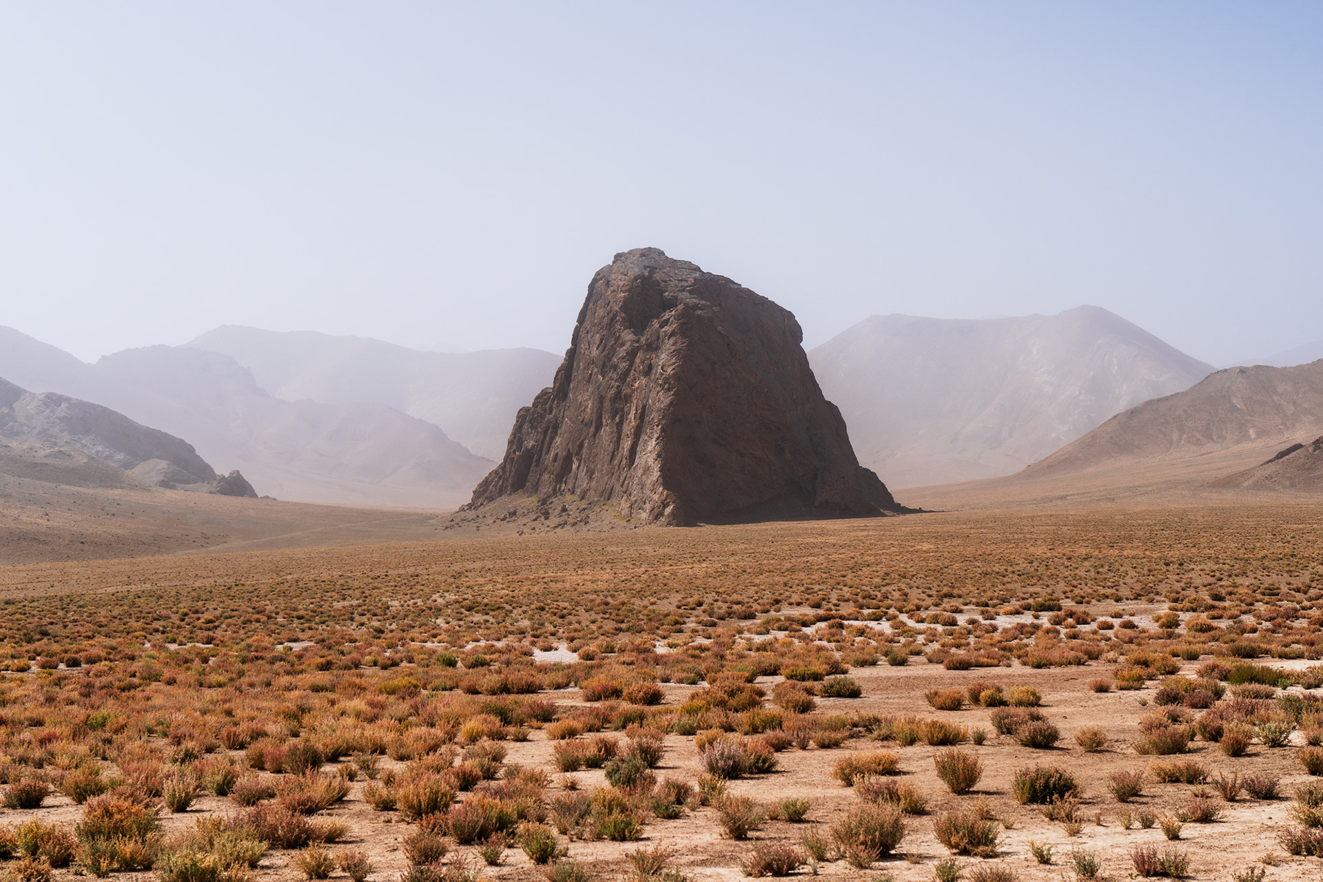 A rugged monolith rises above the Rangkul plateau, hazy morning, Pamir Tajikistan