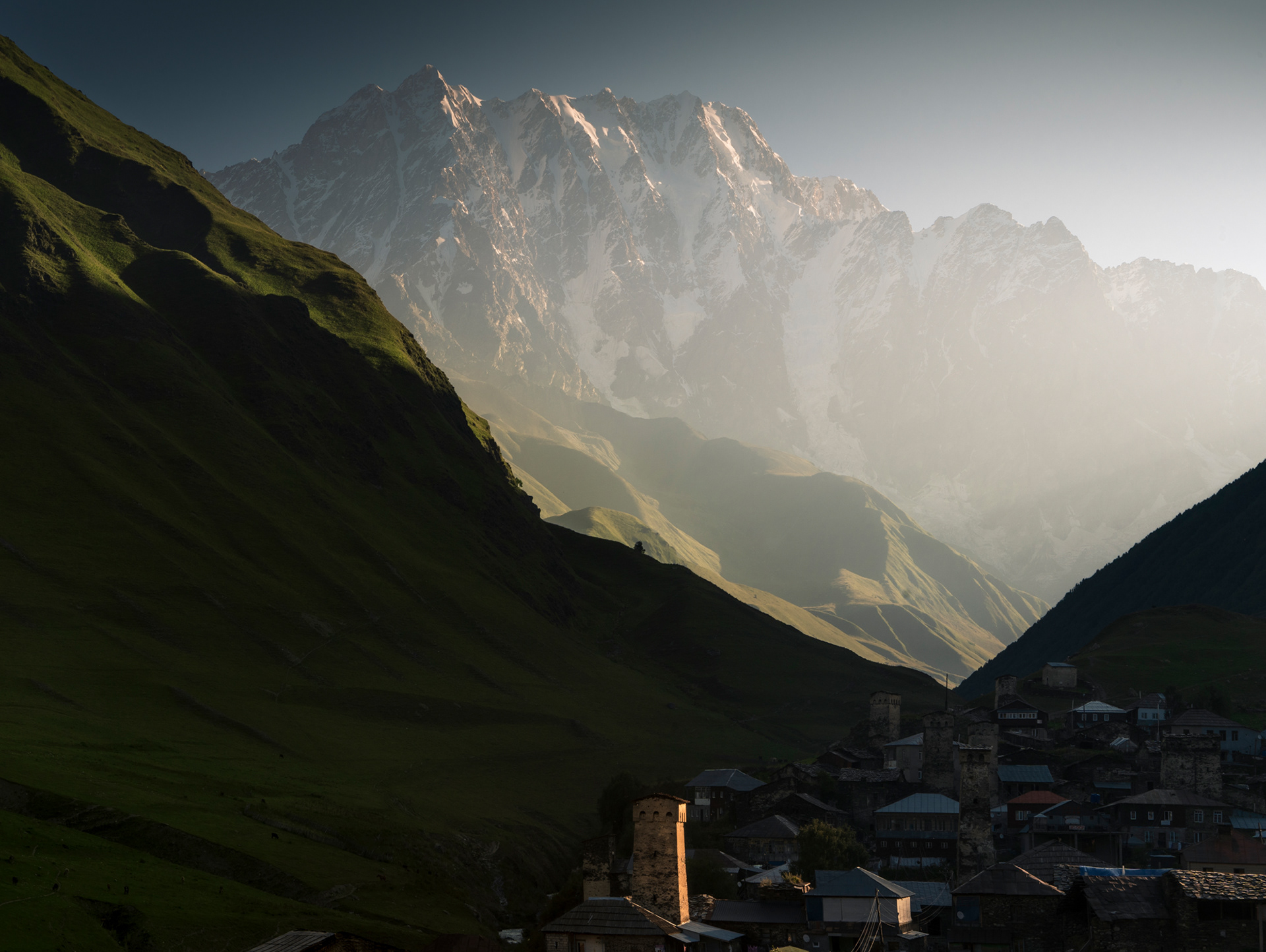 A sunrise over a mountainous village, with ancient defensive stone towers.