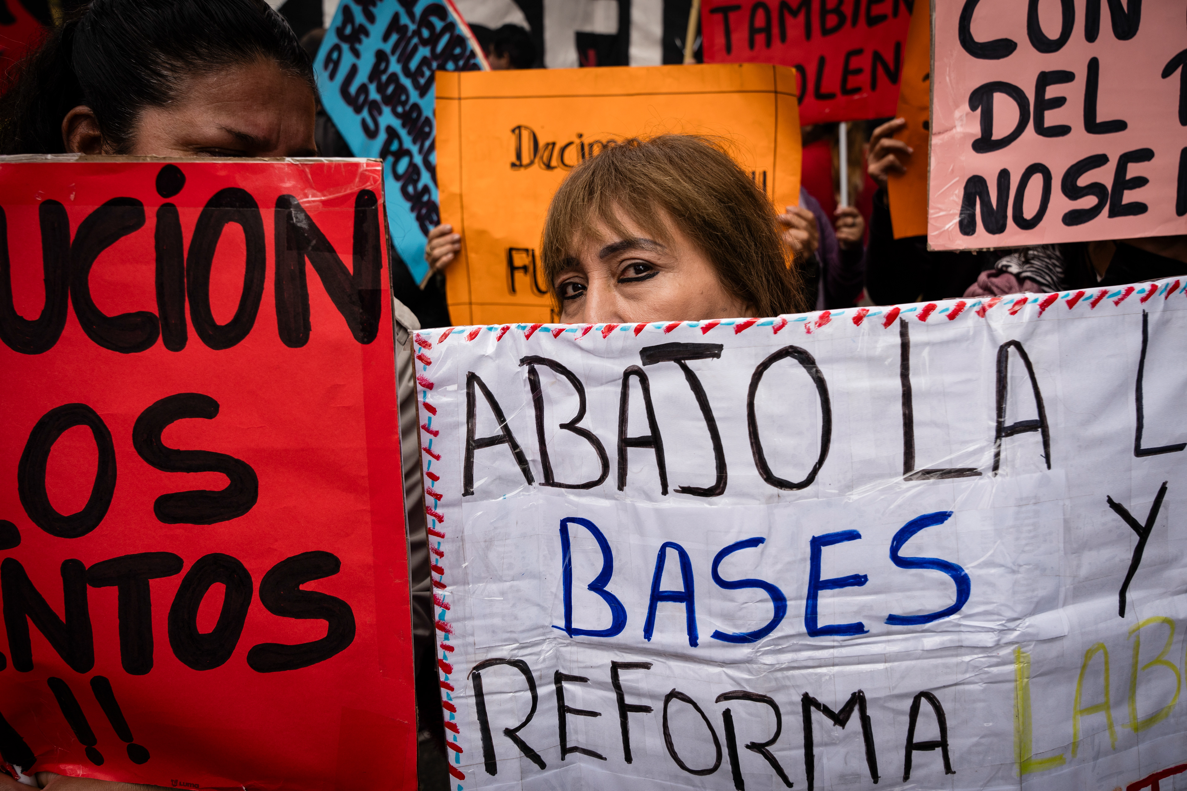 A protester peeks out from behind the banners as they protest outside while the Senate debates Javier Milei's Ley Bases. The Senate Chamber of the Argentine Congress is debating Javier Milei's Ley Bases, which has already passed the Chamber of Deputies. Meanwhile, hundreds of thousands of demonstrators are protesting in the streets, leading to confrontations and repressive actions by security forces, in Buenos Aires, Argentina, on June 12, 2024. PHOTO: Santiago Oroz