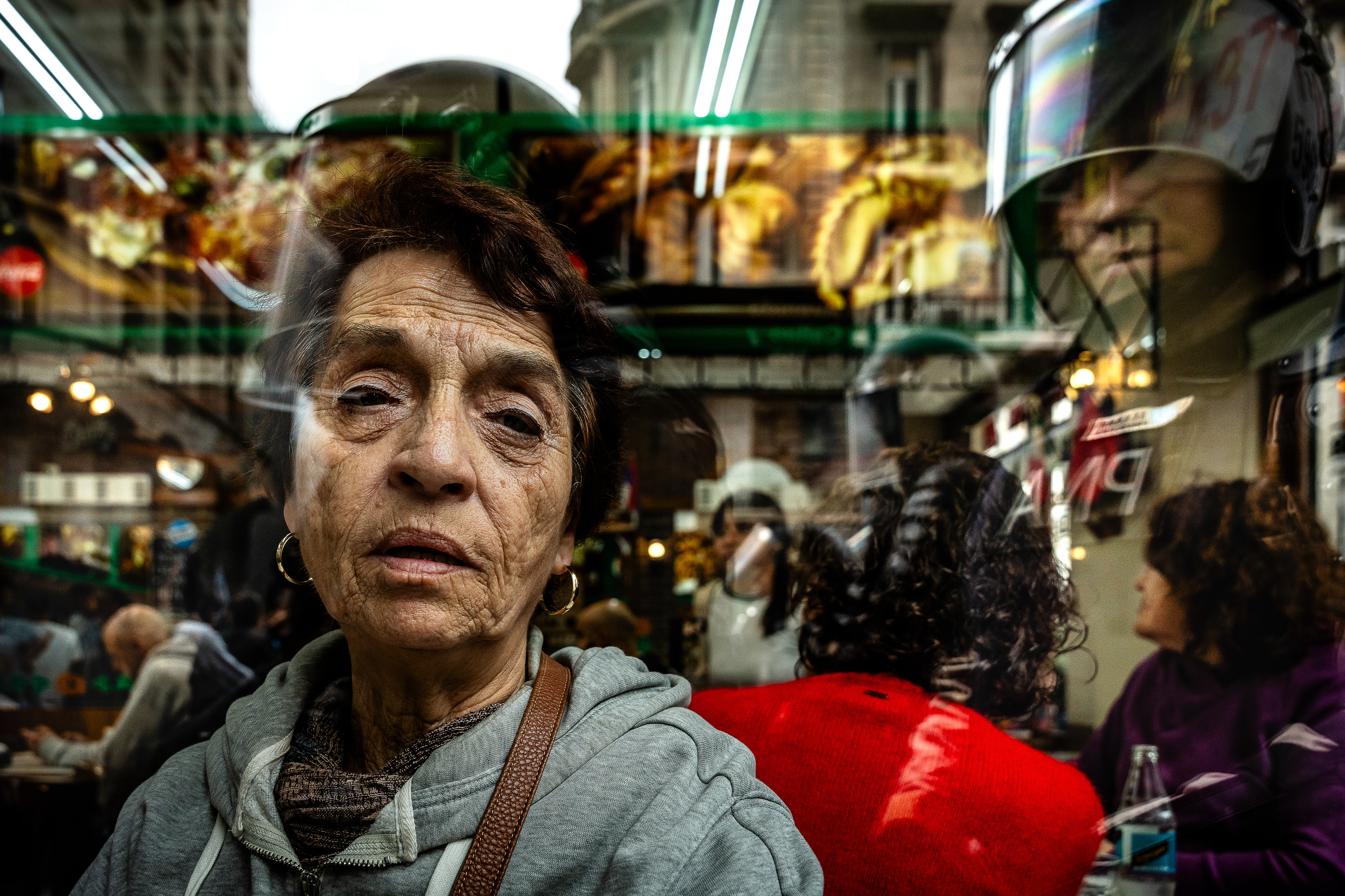 A woman looks at the camera through the glass of a cafe, while being watched by a policeman on the other side. The Senate Chamber of the Argentine Congress is debating Javier Milei's Ley Bases, which has already passed the Chamber of Deputies. Meanwhile, hundreds of thousands of demonstrators are protesting in the streets, leading to confrontations and repressive actions by security forces, in Buenos Aires, Argentina, on June 12, 2024. PHOTO: Santiago Oroz.