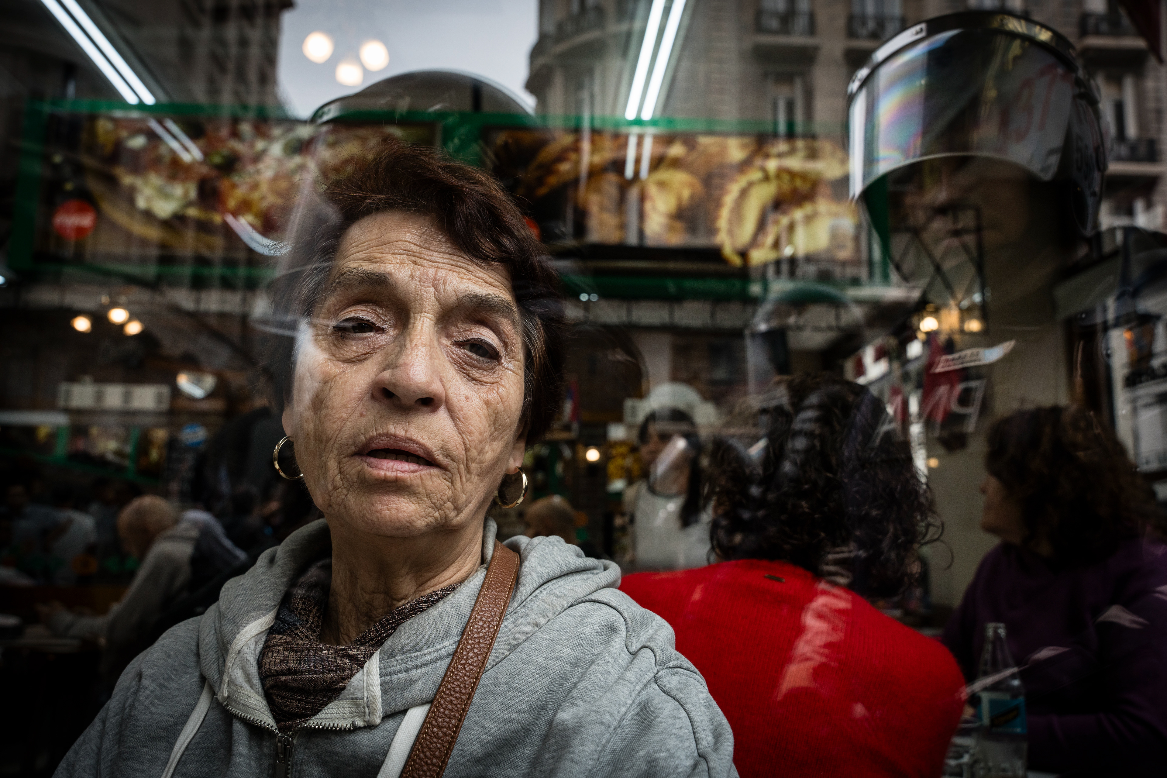 A woman looks at the camera through the glass of a cafe, while being watched by a policeman on the other side. The Senate Chamber of the Argentine Congress is debating Javier Milei's Ley Bases, which has already passed the Chamber of Deputies. Meanwhile, hundreds of thousands of demonstrators are protesting in the streets, leading to confrontations and repressive actions by security forces, in Buenos Aires, Argentina, on June 12, 2024. PHOTO: Santiago Oroz