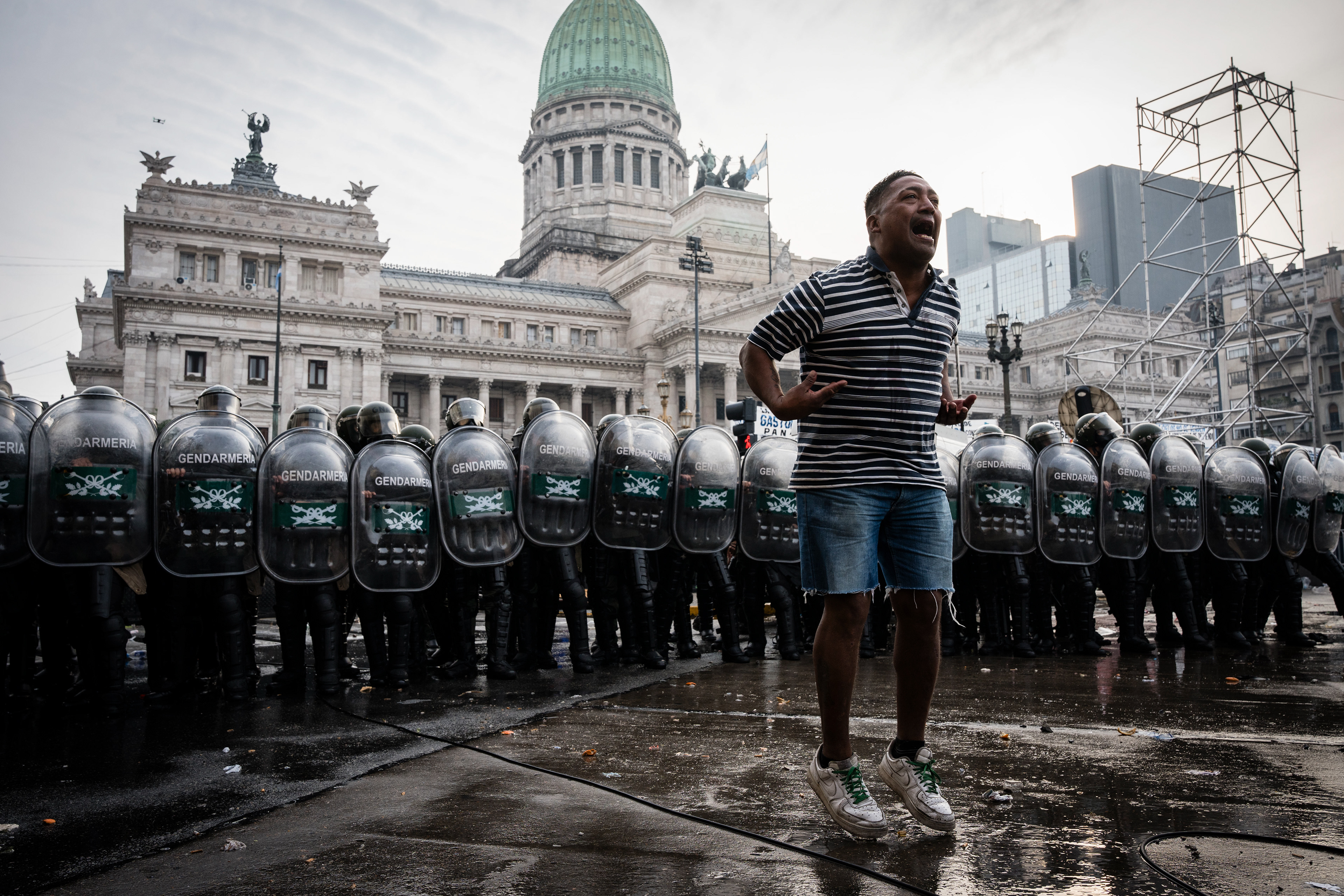 A demonstrator jumps and chants in front of the police line preventing them from advancing toward the National Congress as they protest outside while the Senate debates Javier Milei's Ley Bases. The Senate Chamber of the Argentine Congress is debating Javier Milei's Ley Bases, which has already passed the Chamber of Deputies. Meanwhile, hundreds of thousands of demonstrators are protesting in the streets, leading to confrontations and repressive actions by security forces, in Buenos Aires, Argentina, on June 12, 2024. PHOTO: Santiago Oroz