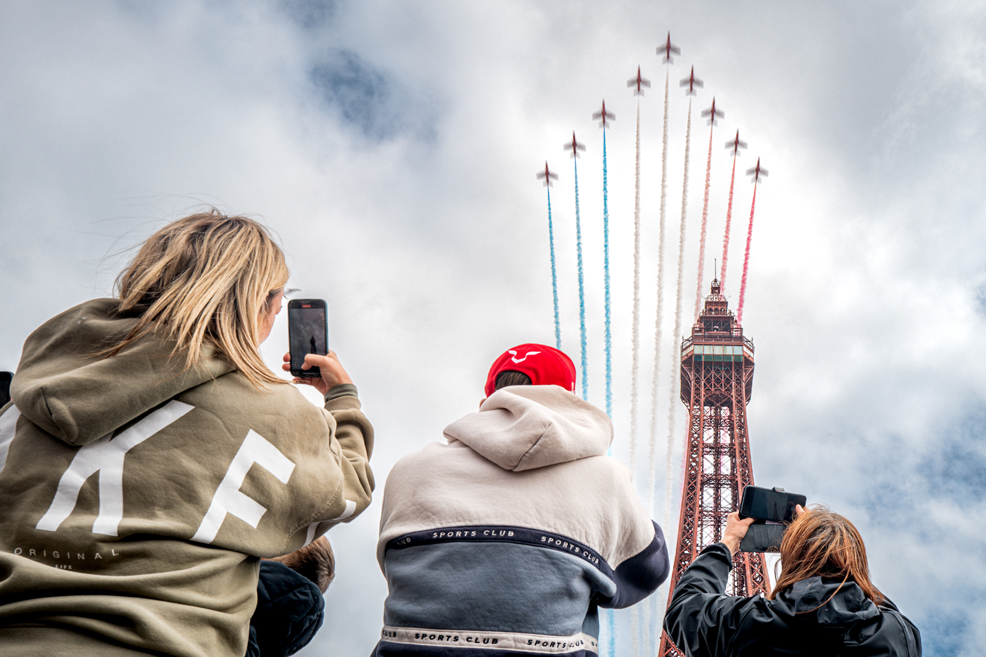 People gather on the Comedy Carpet to watch the Red Arrows fly over the Tower during the Blackpool Air Show in 2025