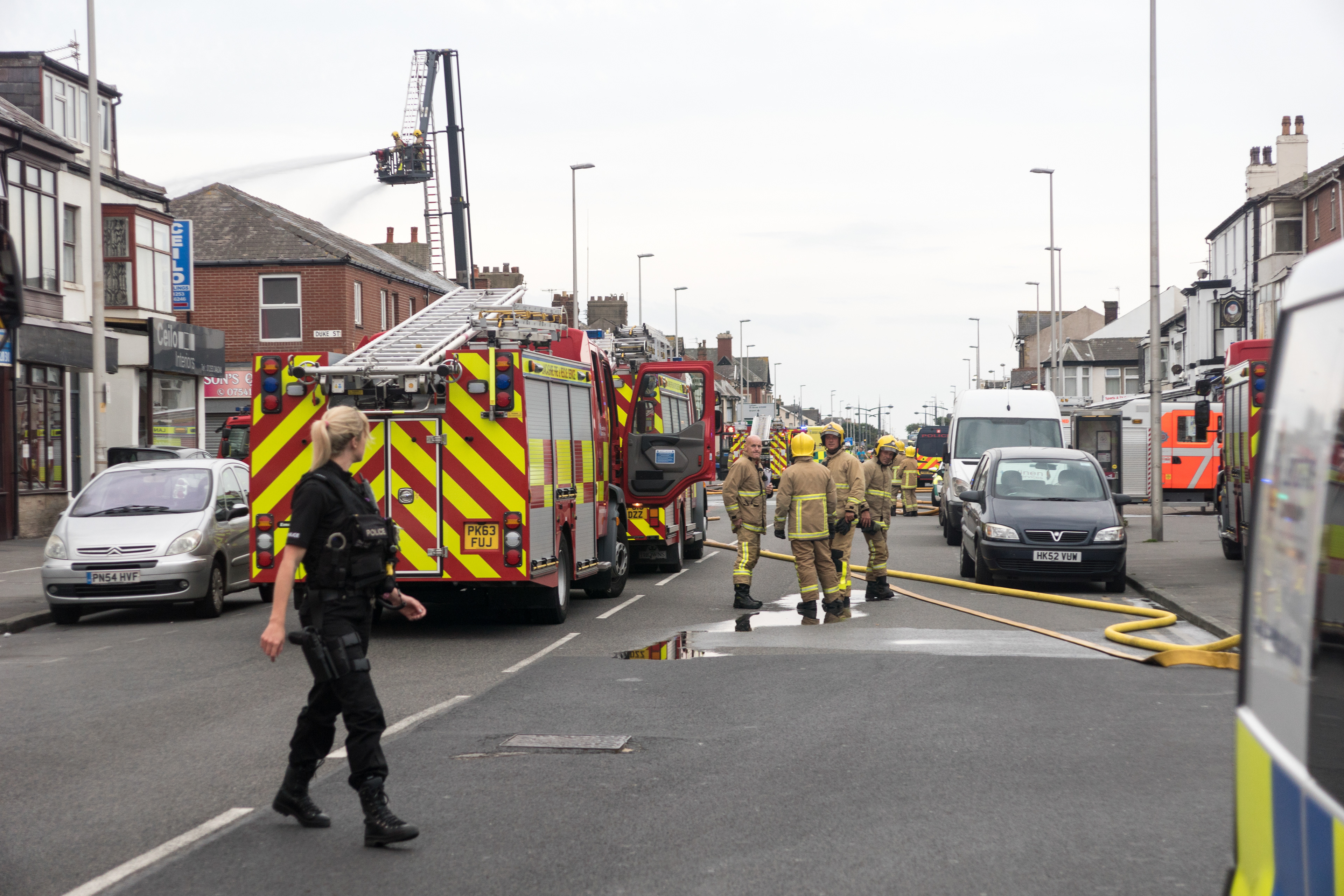 Firefighters look at a passing police officer as a laundry firm burns in Blackpool's South Shore