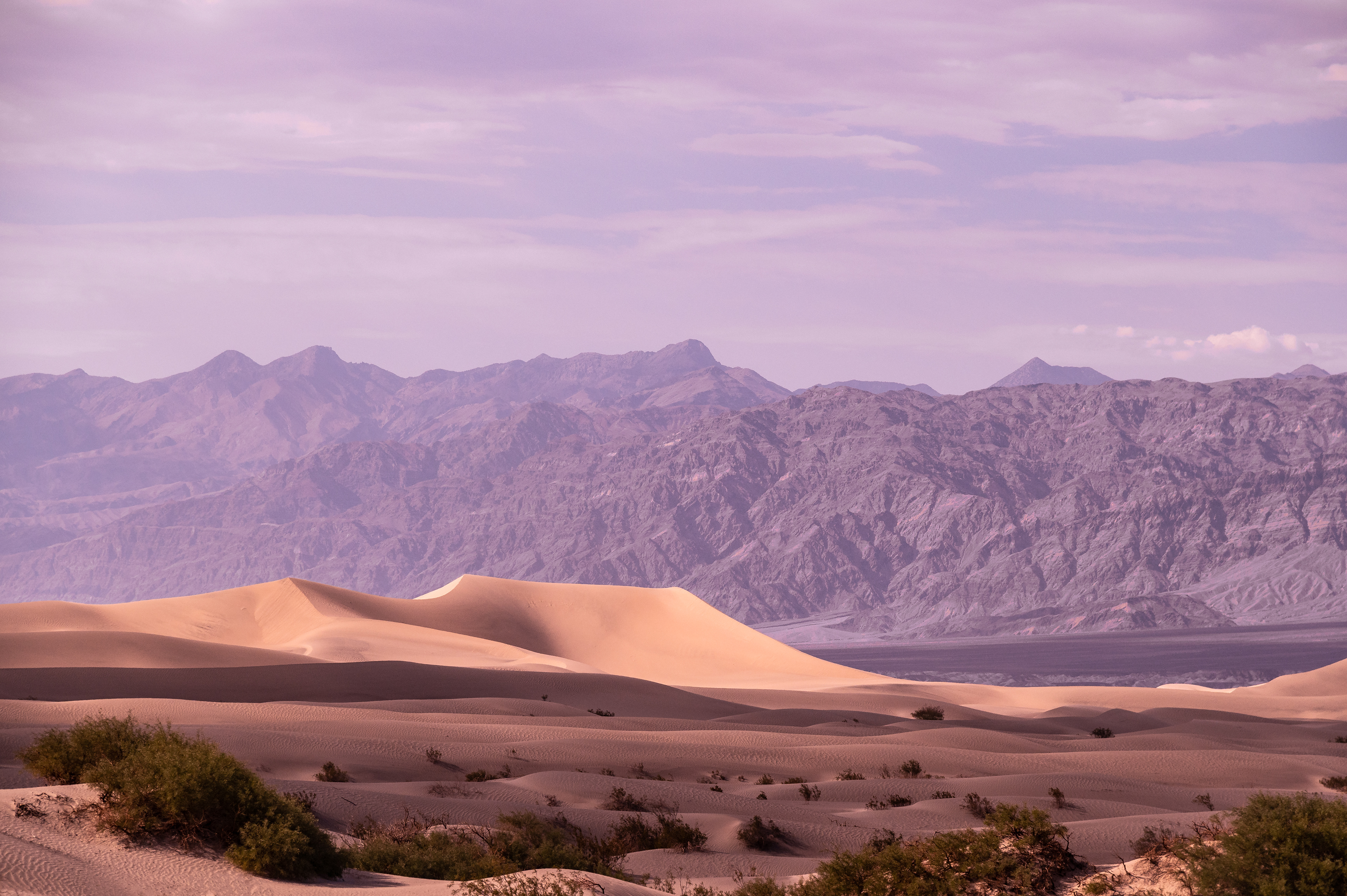 "Passing sunset on Mesquite Flat sand dunes, Death Valley"  Watching as the sun slowly goes down on these sand dunes was perhaps one of the most amazing spectacles from the window of a car.  After travelling from Yosemite through to Death Valley national park it was insane to see the change of scenery. Driving up winding roads to some of the many 7000ft peaks before going down to below sea level was a captivating sight.  After travelling for a couple of hours the winding roads came to a halt, and across one of the many valley floors the Mesquite Flats stuck out like a sore thumb. The juxtaposition between hard Mars like rock in the background and the soft and ever changing sand dunes in the foreground came out as an interesting composition to take advantage of.  These dunes rise to only 100 feet, their constantly changing forms contrasting the some 1.7 billion year old rocks in many of the Death Valley mountain ranges.
