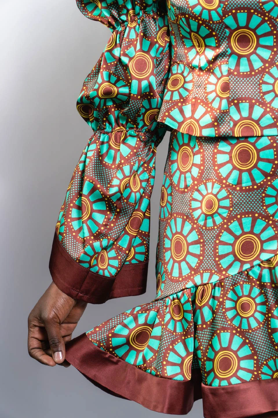 detalle de la parte inferior de un vestido de tela satinada tipo seda estampado con un diseño de estilo africano en colores bordeaux, turquesa y amarillo