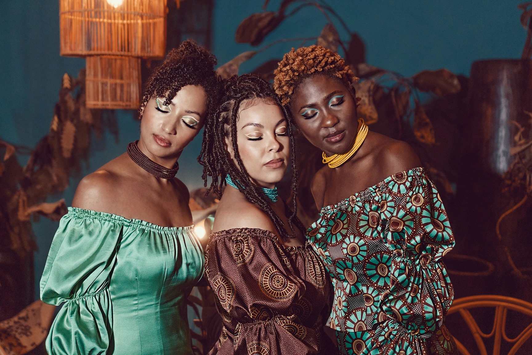 Tres mujeres con los ojos cerrados juntando sus cabezas, usan el mismo vestido con distintos estampados con motivos digitales inspirados en las telas africanas conocidas como shweshwe que se realizan con una técnica artesanal