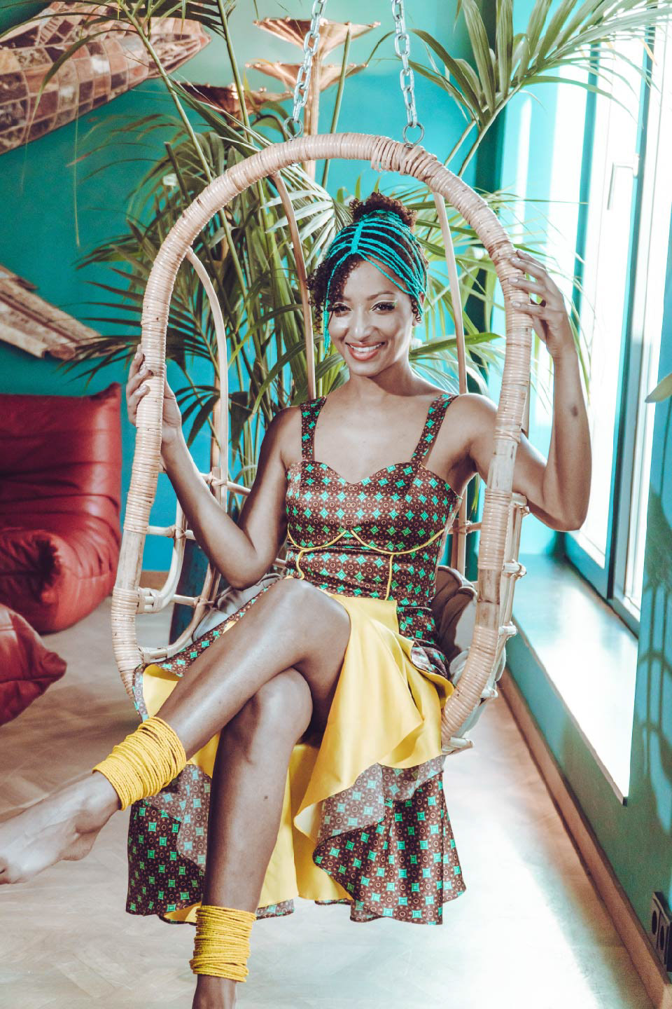 mujer sonriendo, sentada en una hamaca, usando un vestido estampado con diseño de inspiración africana en colores turquesa, bordeaux y amarillo