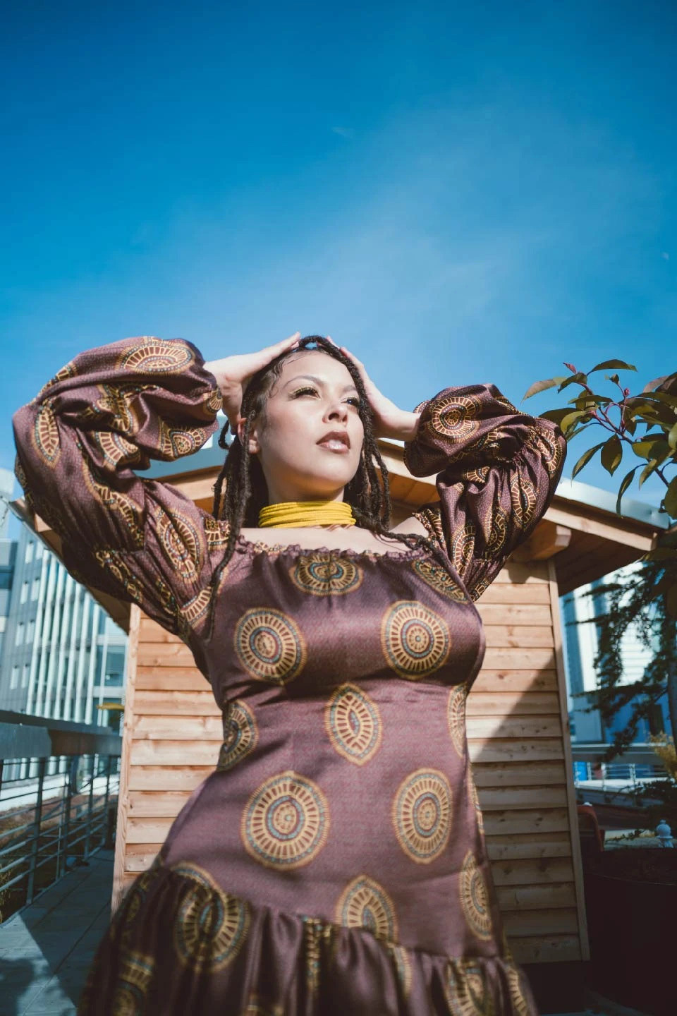 Mujer mirando al sol luciendo un vestido estampado con un diseño de estilo africano, en colores bordeaux, amarillo y detalles en turquesa