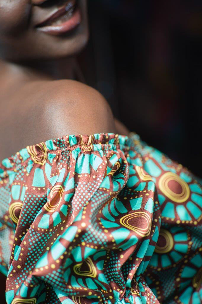 detalle de la parte superior del escote y manga de un vestido de tela satinada tipo seda estampado con un diseño de estilo africano en colores bordeaux, turquesa y amarillo