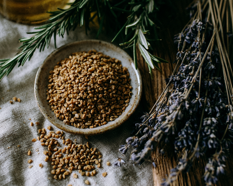 small bottle of castor oil, fenugreek seeds in a small dish and scattered loosely, a sprig of rosemary and a few dried lavender stems