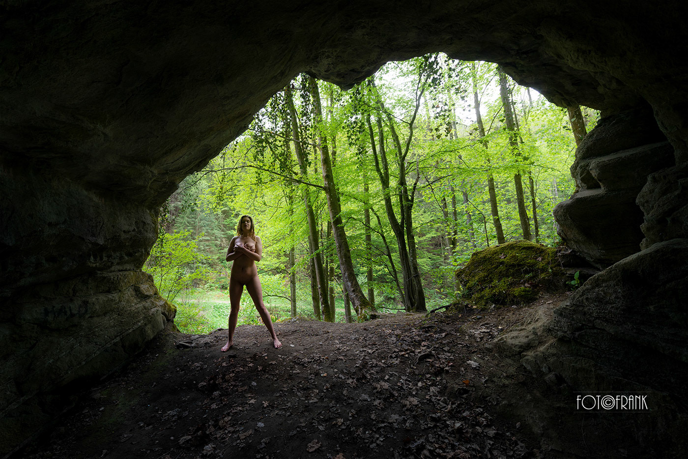 Frauenakt steht verbunden mit der Natur am Höhleneingang der Steinzeithöhle "Gudenoshöhle" im Waldviertel von Niederösterreich