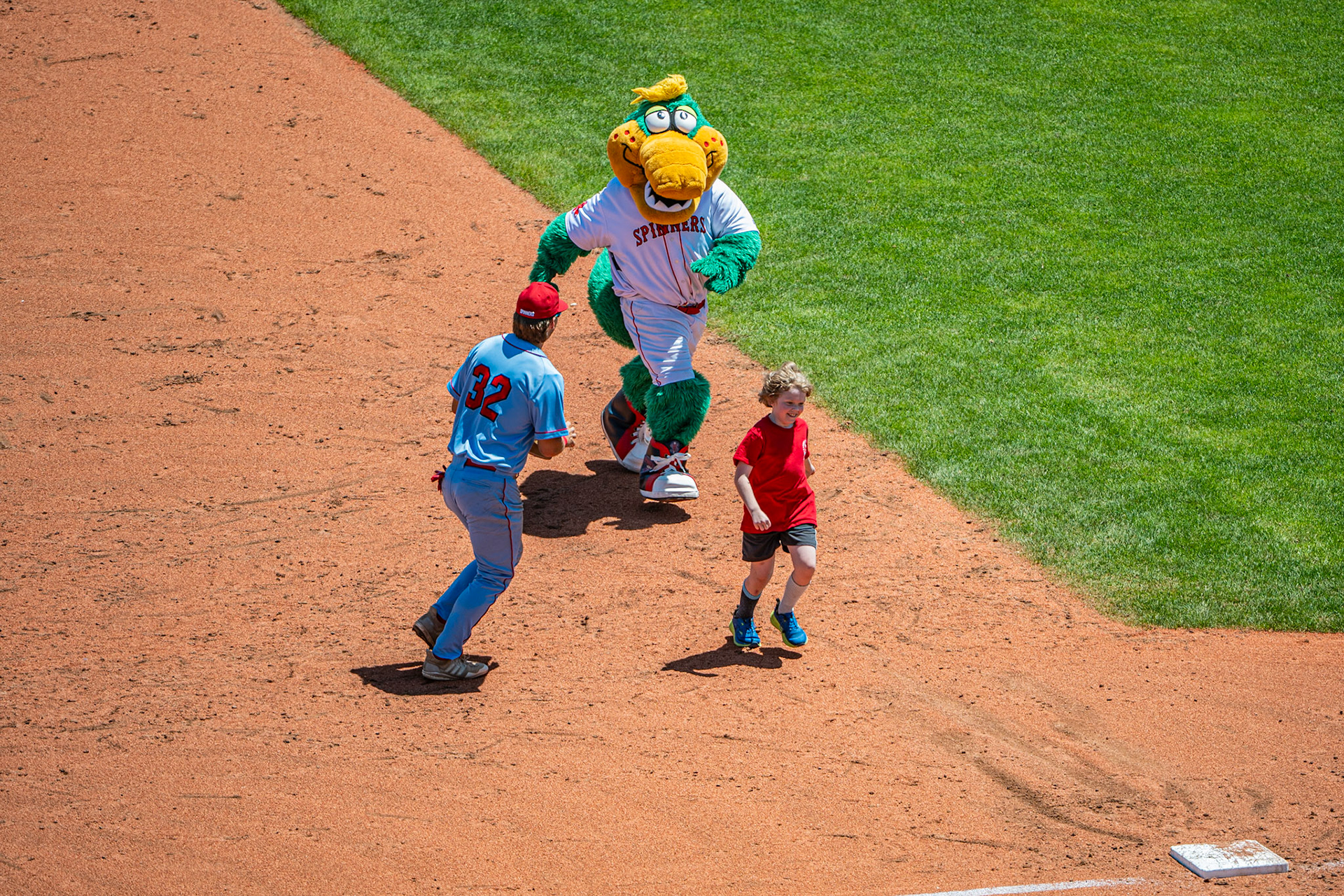 A young Lowell Spinners fan races the team mascot, "Canalagator" during an intermission as Spinners' player Ryan O'Leary watches closely. The game was played at Edward A. LeLacheur in Lowell, MA, on June 8th, 2026.