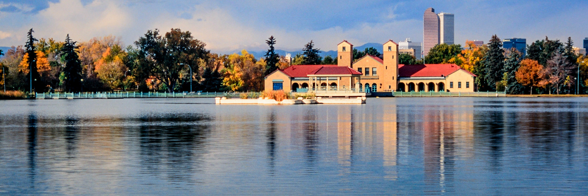 City Park, one of the oldest public spaces in Denver, was designed and built before the turn of the twentieth century, and the park is currently home to the Denver Zoo and the Denver Museum of Nature and Science. The loop around Ferril Lake provides lovely views of the trees around the lake. Captured just after sunrise, the Boathouse, Pavilion, Prismatic Fountain, colorful trees, and two of Denver’s tallest buildings are reflected in the calm water of the lake. A faint Mount Blue Sky (formerly Mt. Evans) , somewhat obscured by the clouds, may be seen in the skyline above the trees immediately to the left of the boathouse. (Unable to confirm the name of the mountain located between the two towers of the boathouse.)
