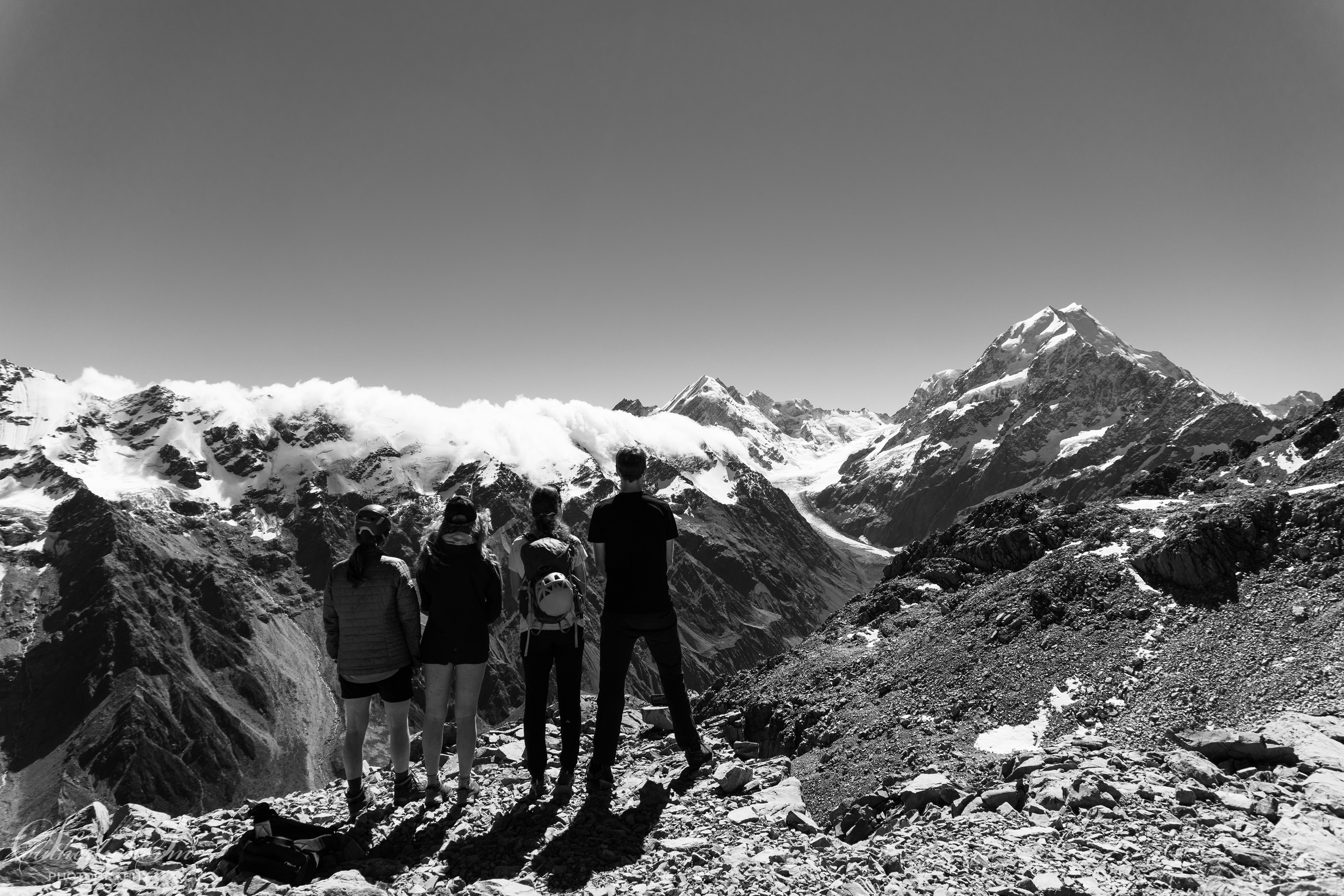 Black and white of four climbers admiring the view of Mt Cook Aoraki, as the clouds come over the range