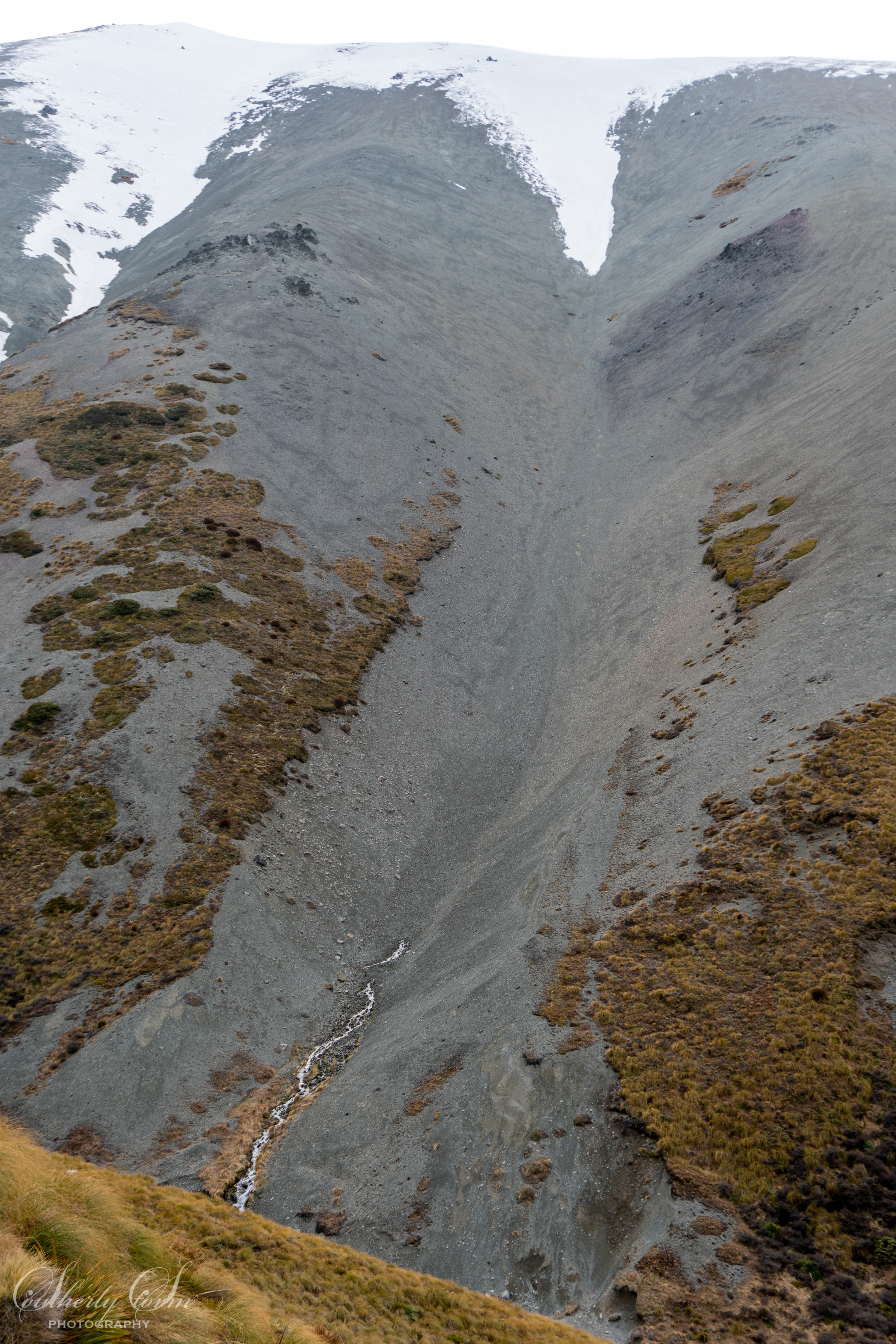 Gravel gully with snow at the top, and a creek arising from the gravel part way down