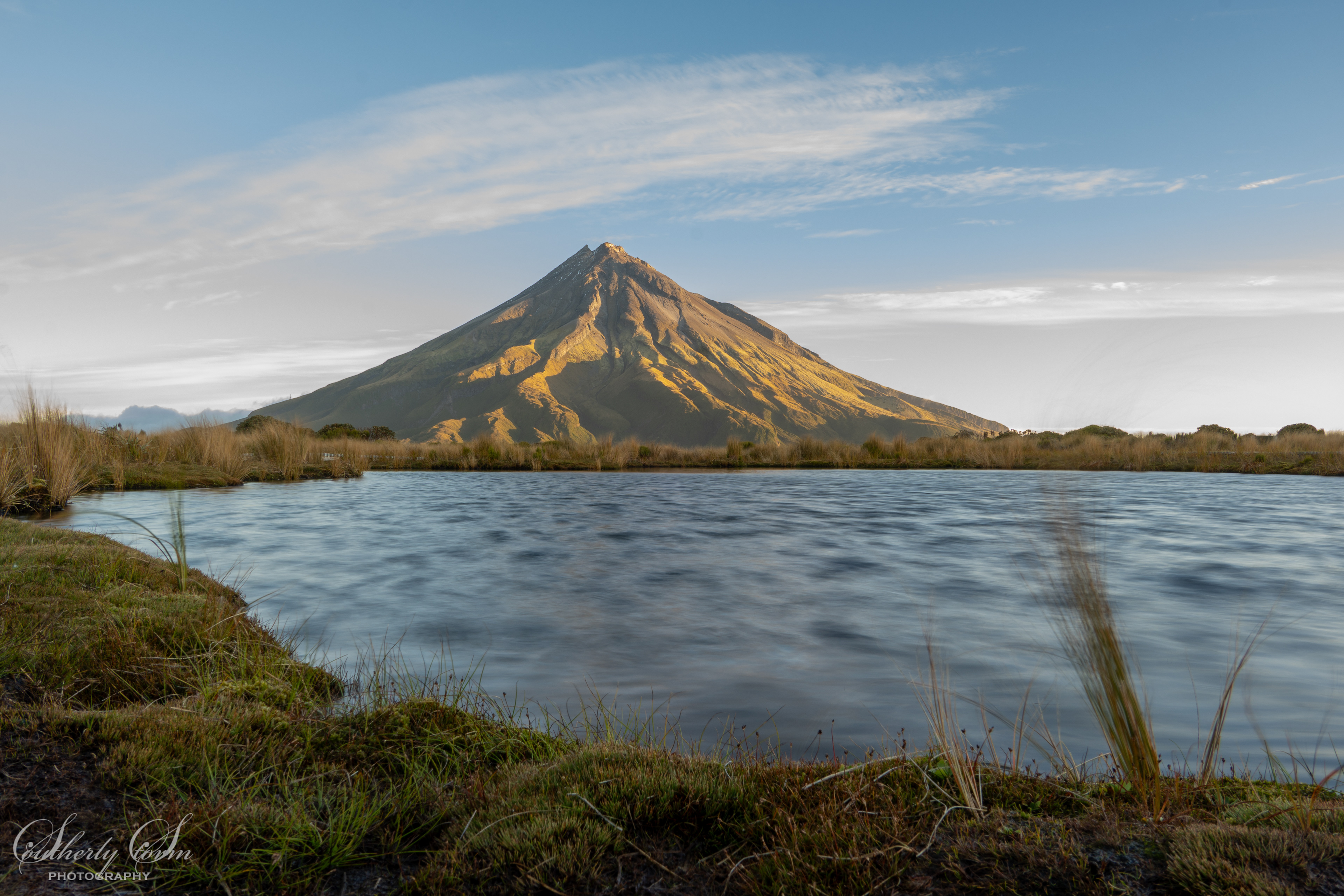 Evening light on Mt Taranaki over a textured Pouakai Tarn