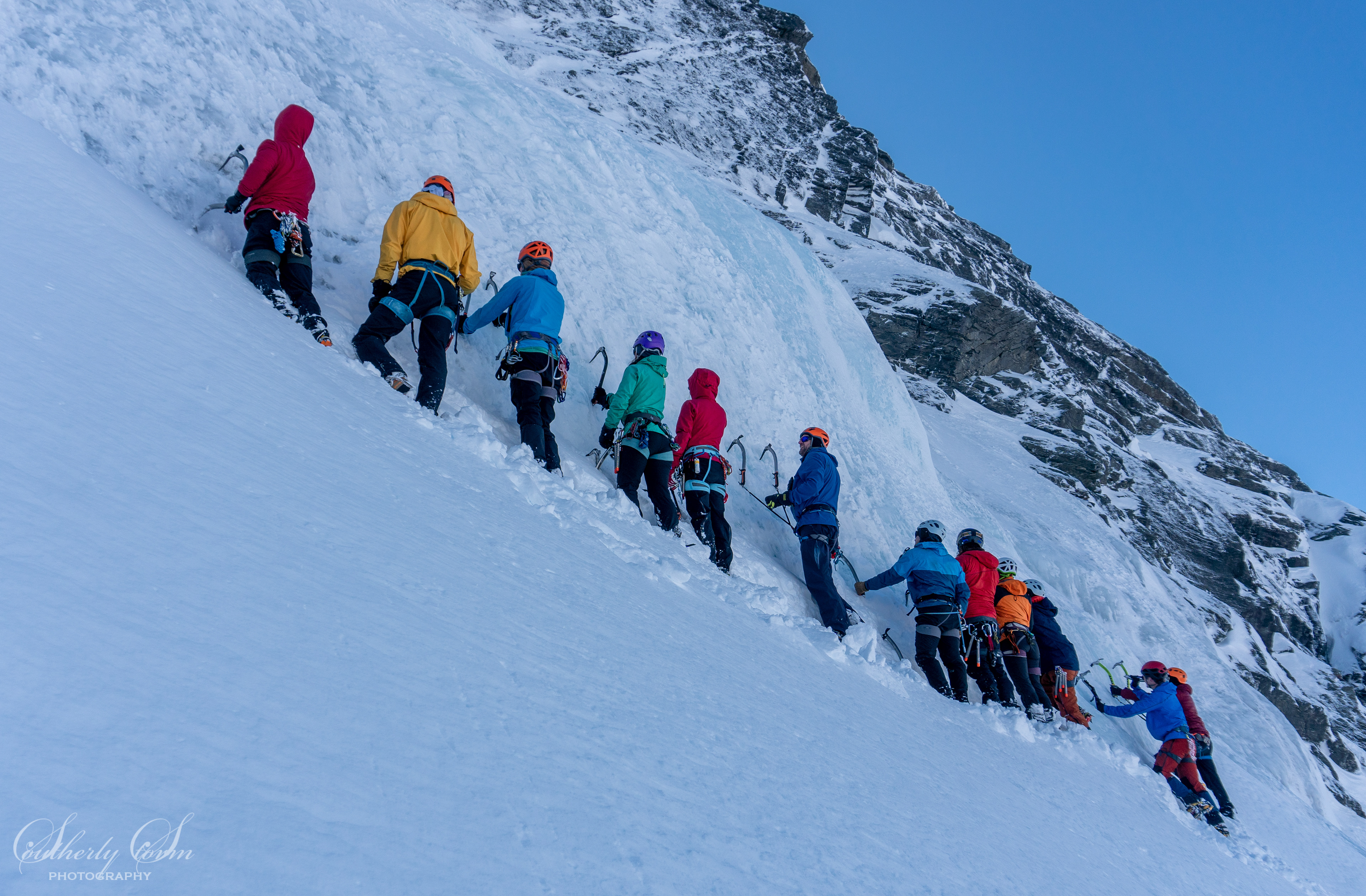 Colourful climber lined up at the base of the ice, learning to use tools