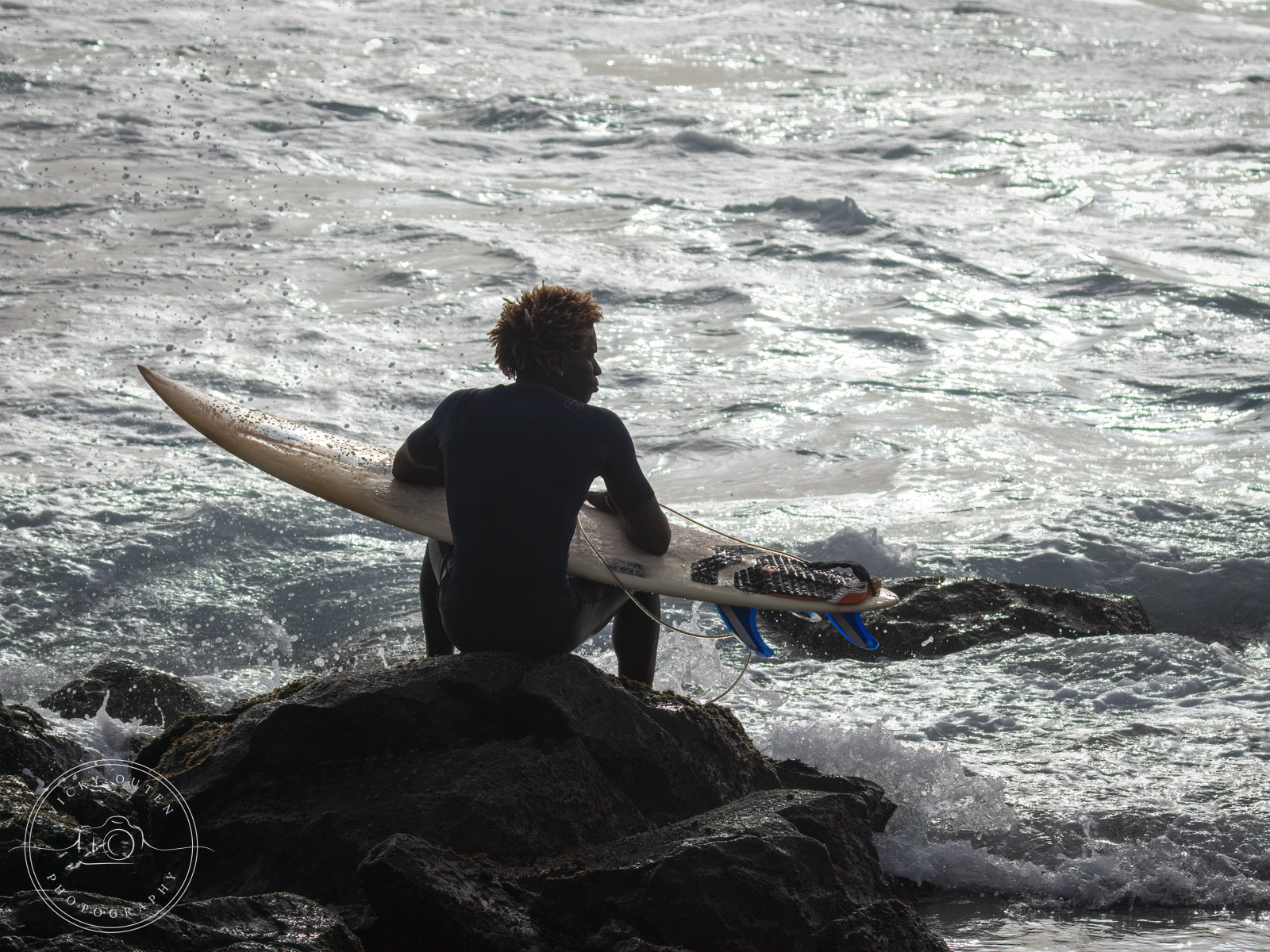 Backlit surfer sitting on the rocks