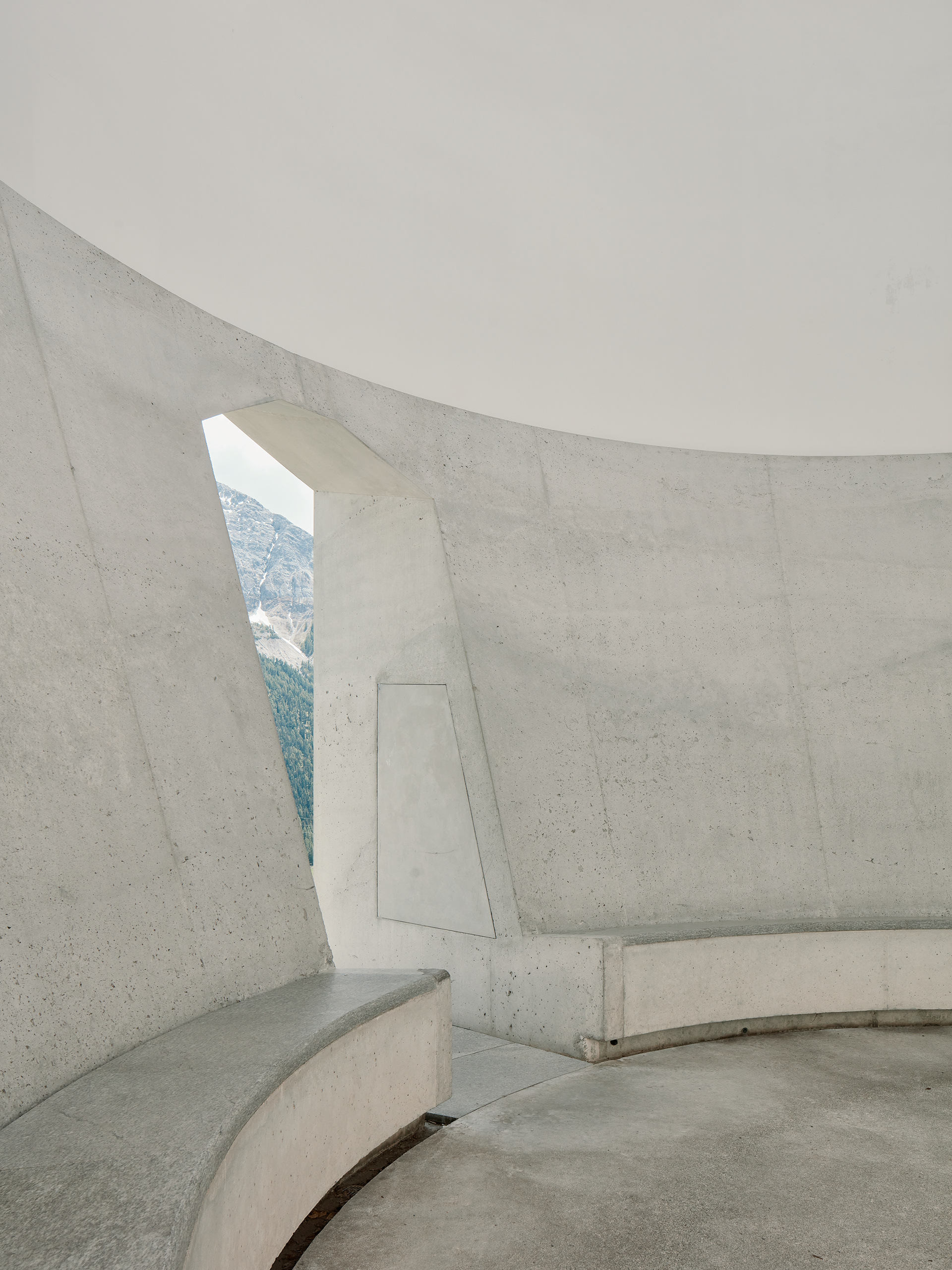 Detail at James Turrell's Skyspace right next to Hotel Castell in Zuoz, Switzerland. Highlighting the materiality of the concrete and the architectural feeling of the space the image only shows the minimalist curve of the sitting area from which visitors are invited to look up into the sky plus a slice of the view to the outside through the cut-out concrete portal.