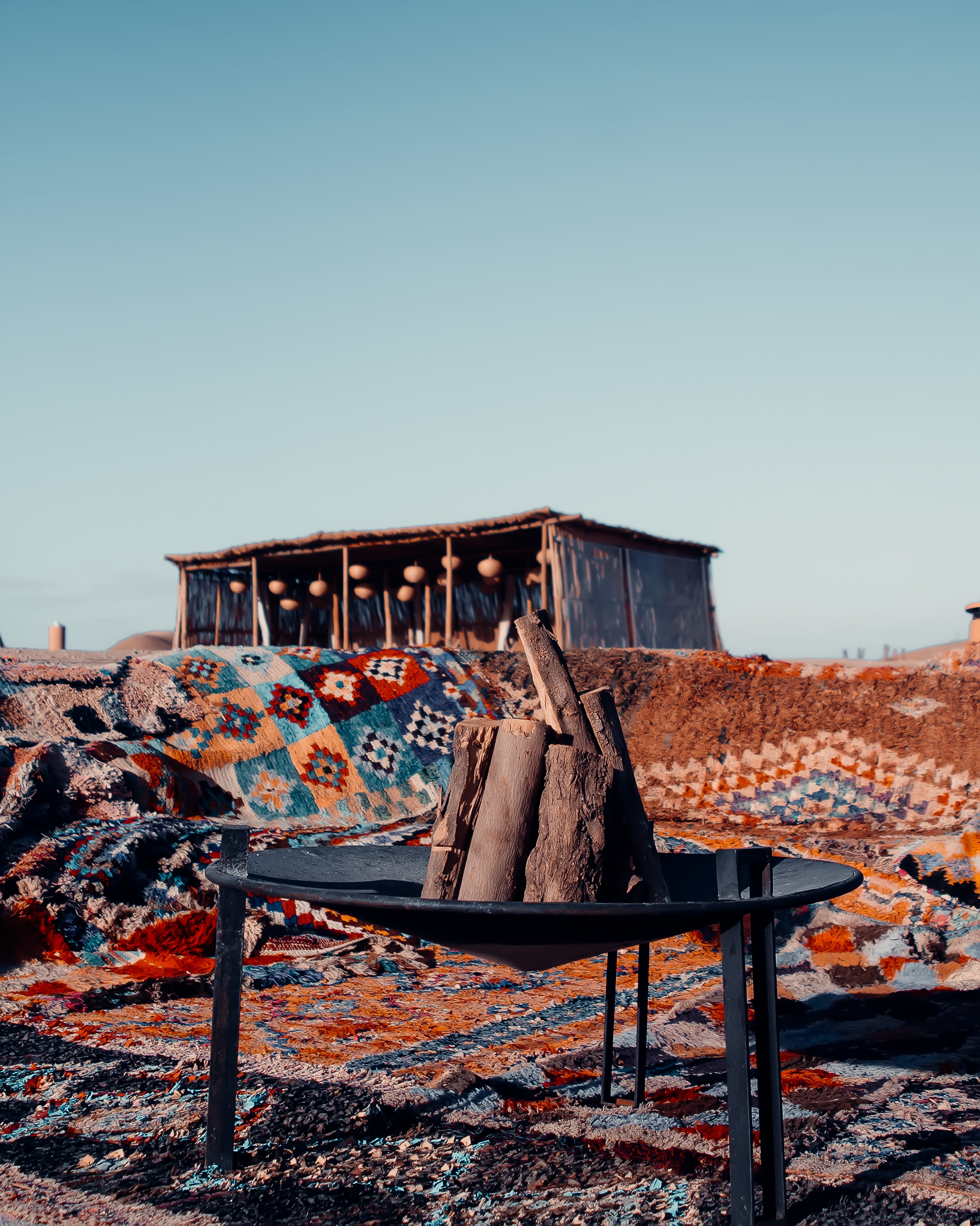 Temlyder — hospitality photography, outdoor desert lounge area with fire pit and traditional Moroccan rugs, luxury camp visual