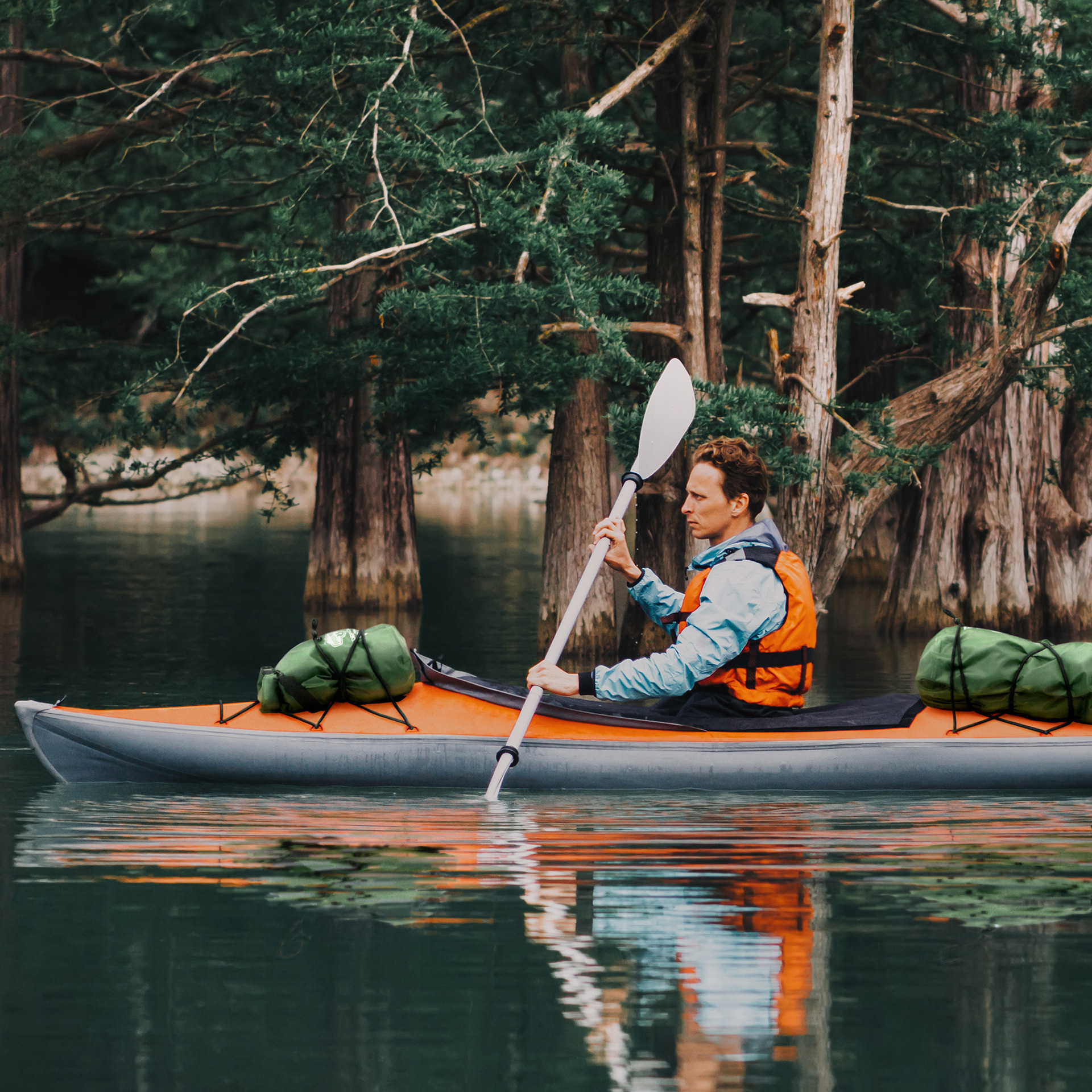 Added dry bags and their reflections onto photo of man kayaking.