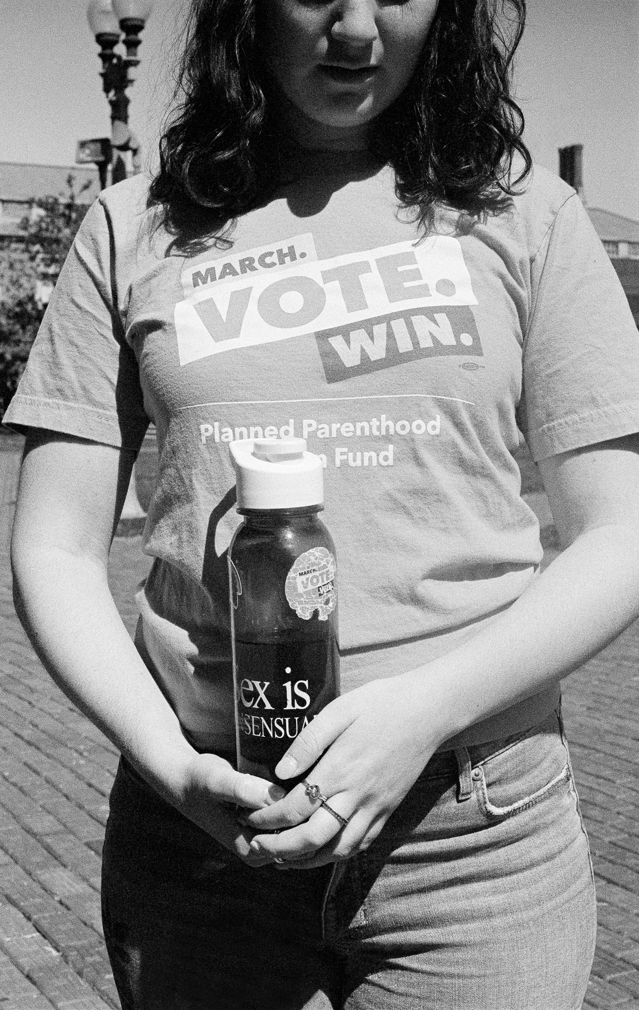 A woman in a "March. Vote. Win." Planned Parenthood t-shirt holding a "Sex is consensual" water bottle with a faded Planned Parenthood "VOTE" sticker on it