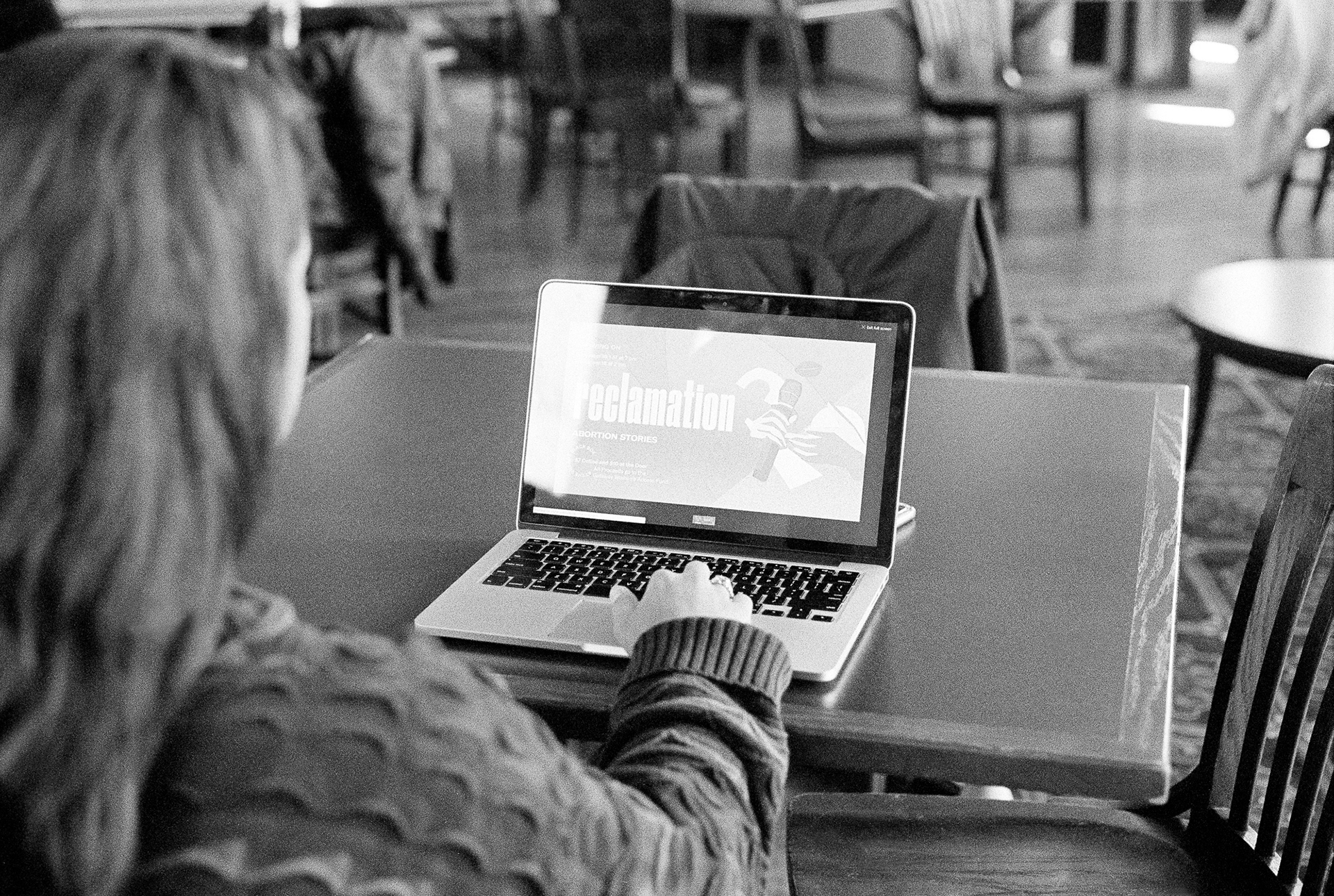 Woman working on a laptop, with her screen open to a graphic that reads "reclamation: abortion stories"