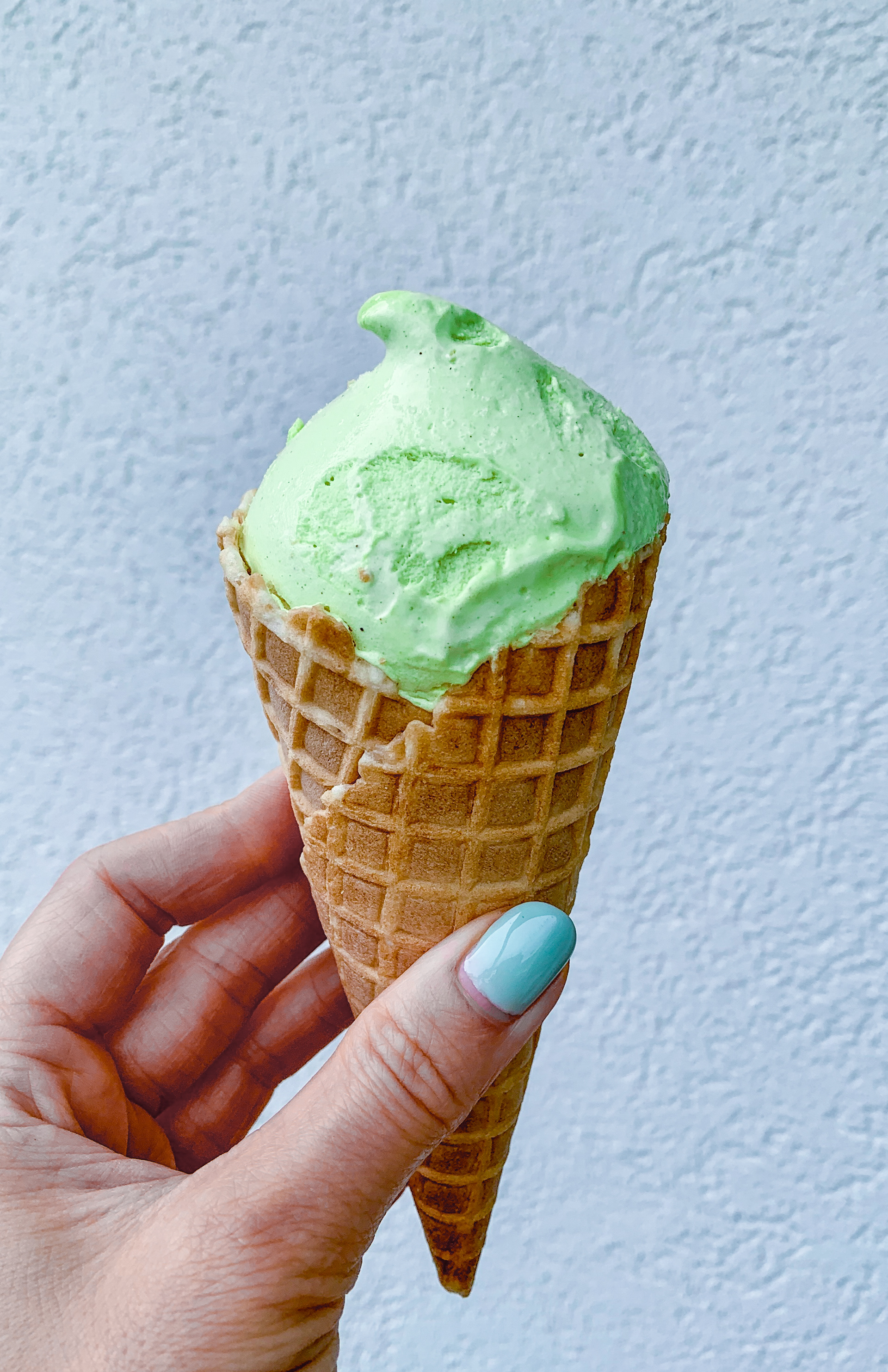 Pistachio ice cream cone in a hand, at a light gray textured background