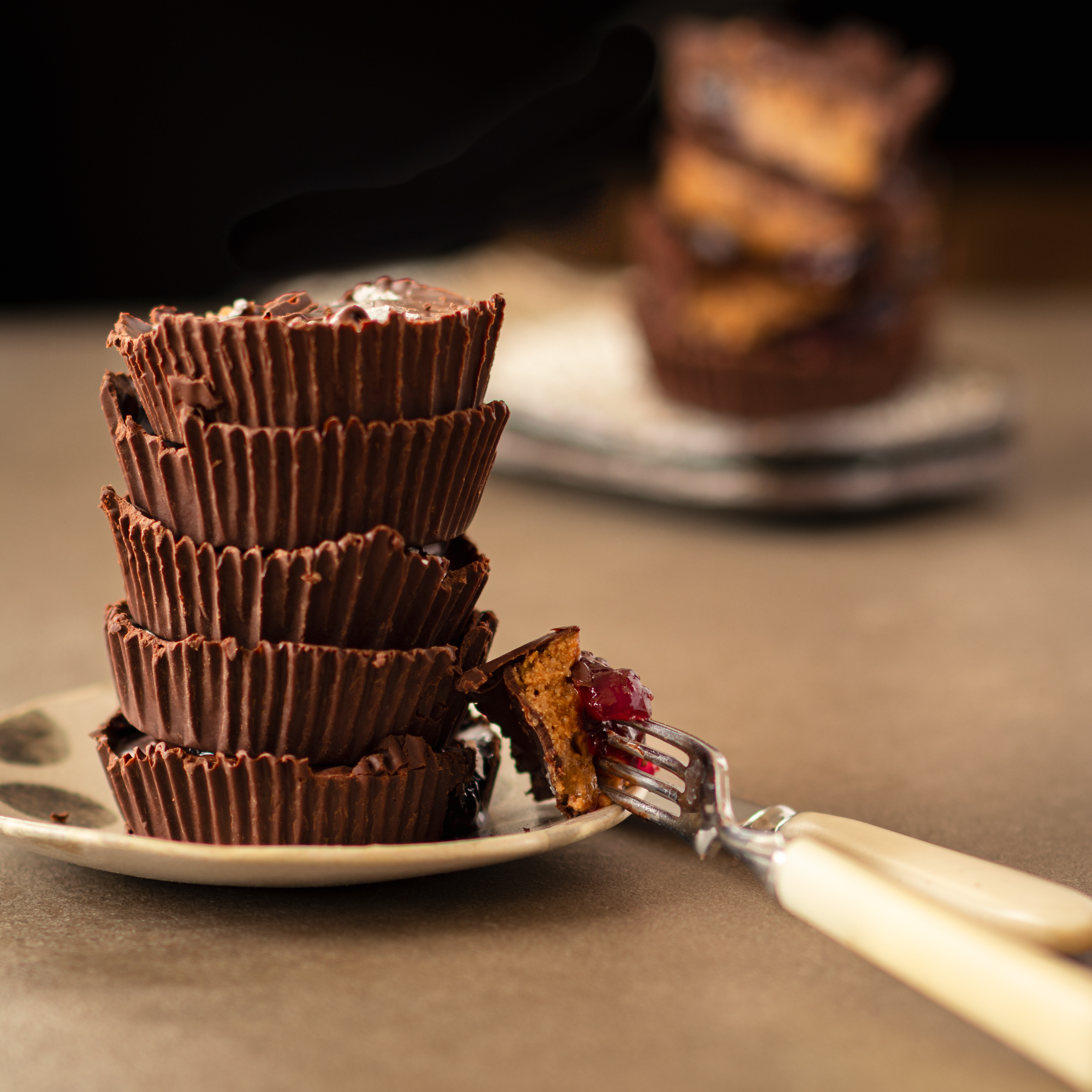 Stacked homemade dark chocolate sunflower seed butter cups on a small plate, with one cut open showing a creamy seed butter filling and a layer of jam, soft natural lighting and blurred background