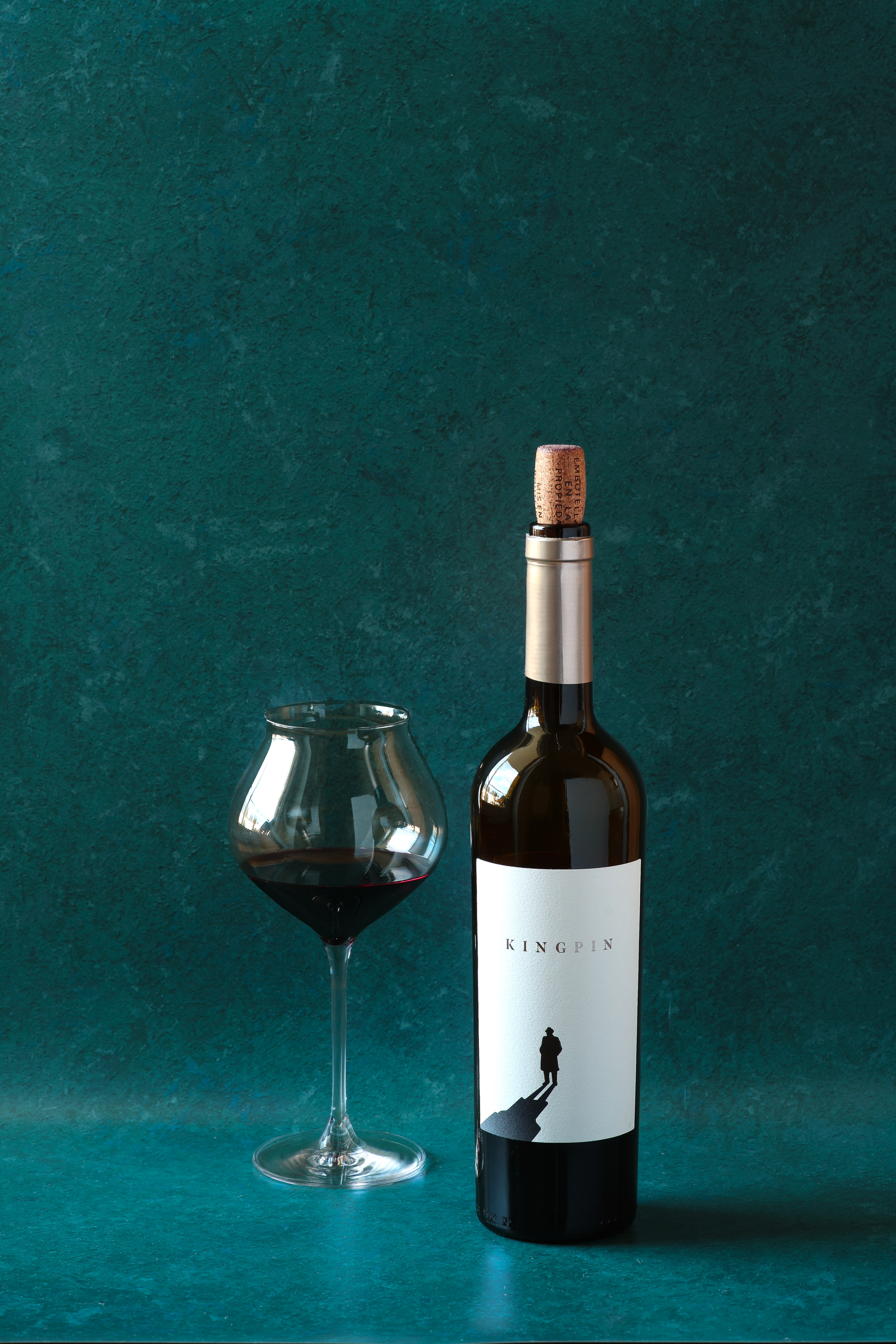 Red wine glass and bottle on a dark forest green background