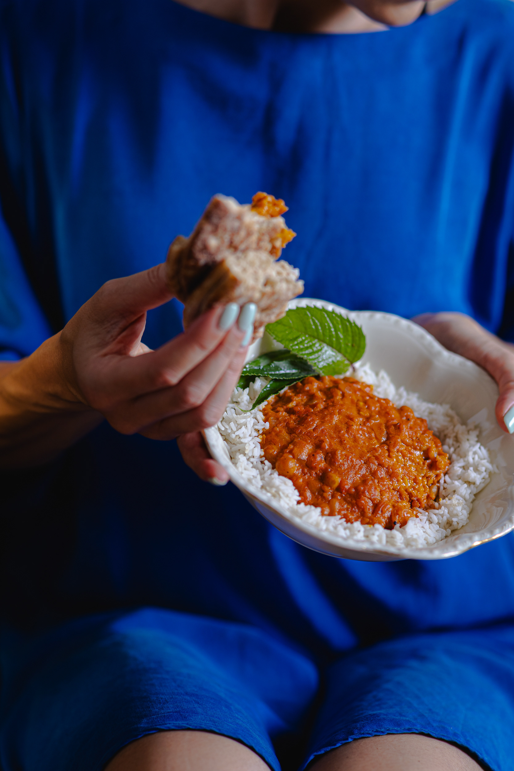 Woman in blue dress eating vegan coconut chickpea curry