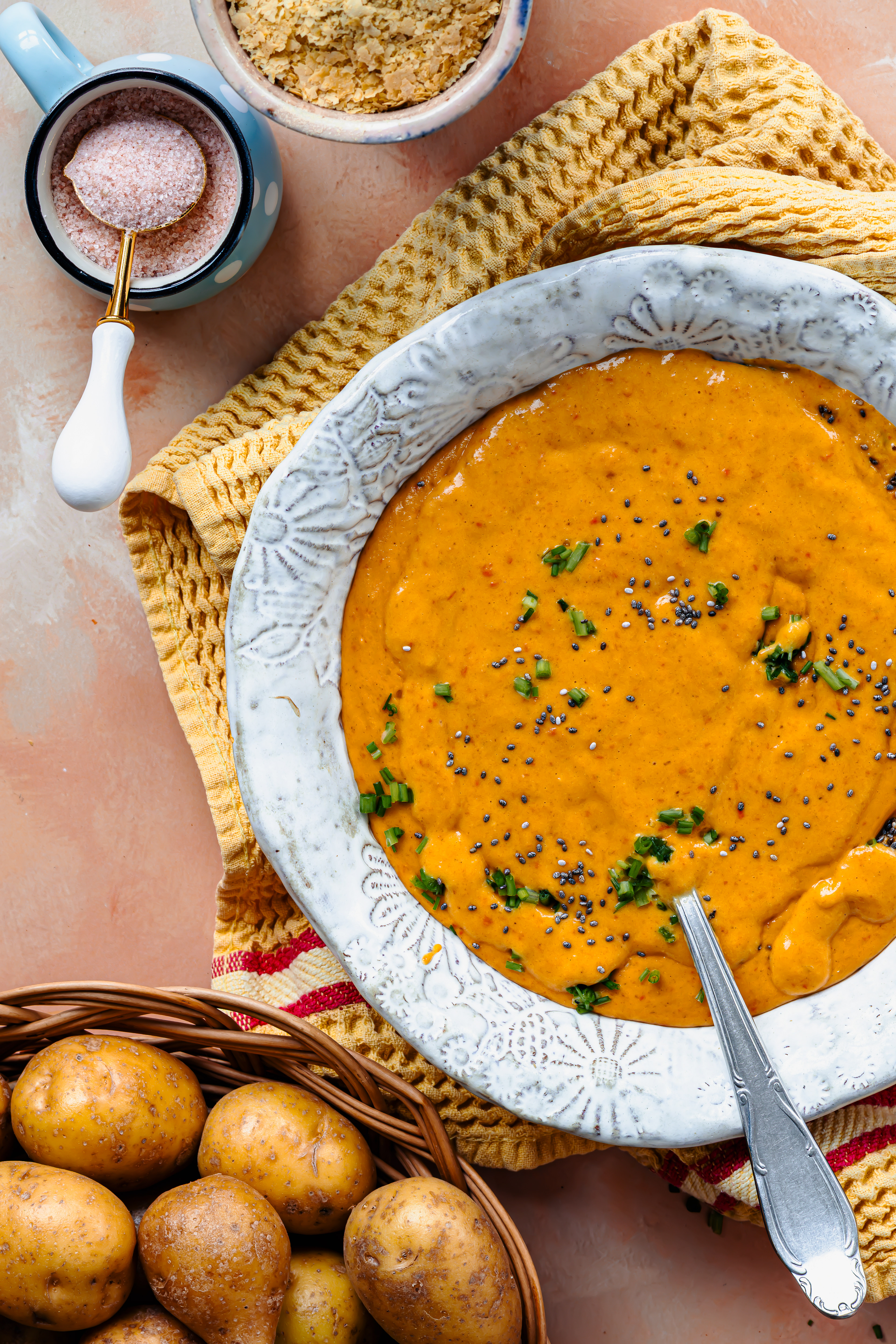 Vibrant dark yellow vegetable cream soup placed on a yellow towel and on a light orange teel backdrop