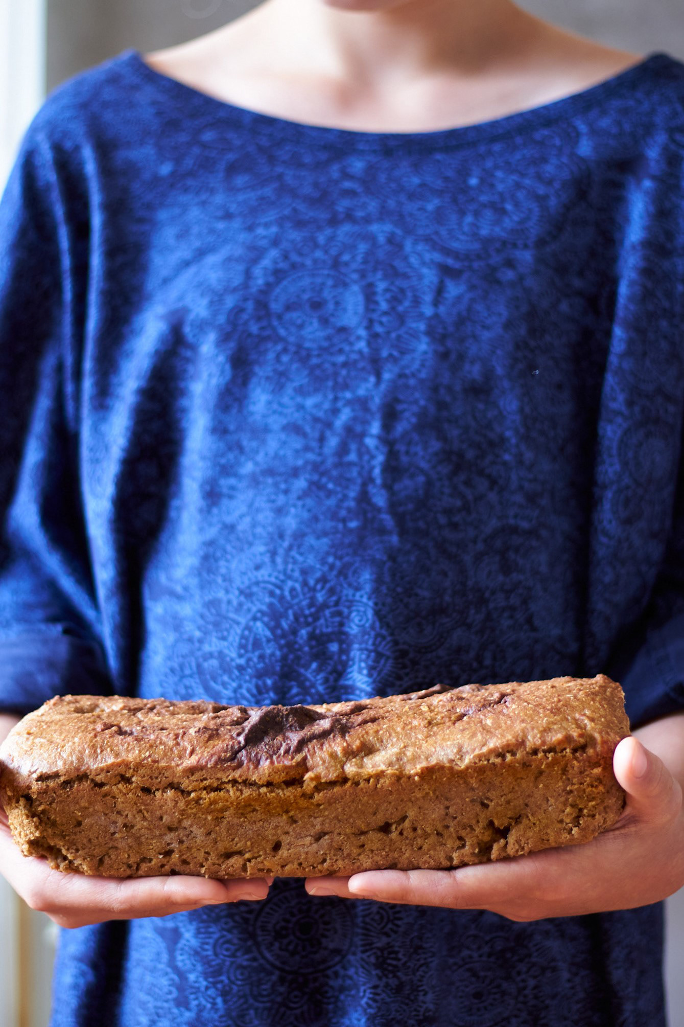 Girl in large royal blue shirt - standing and holding a rye bread. Very Nordic vibe