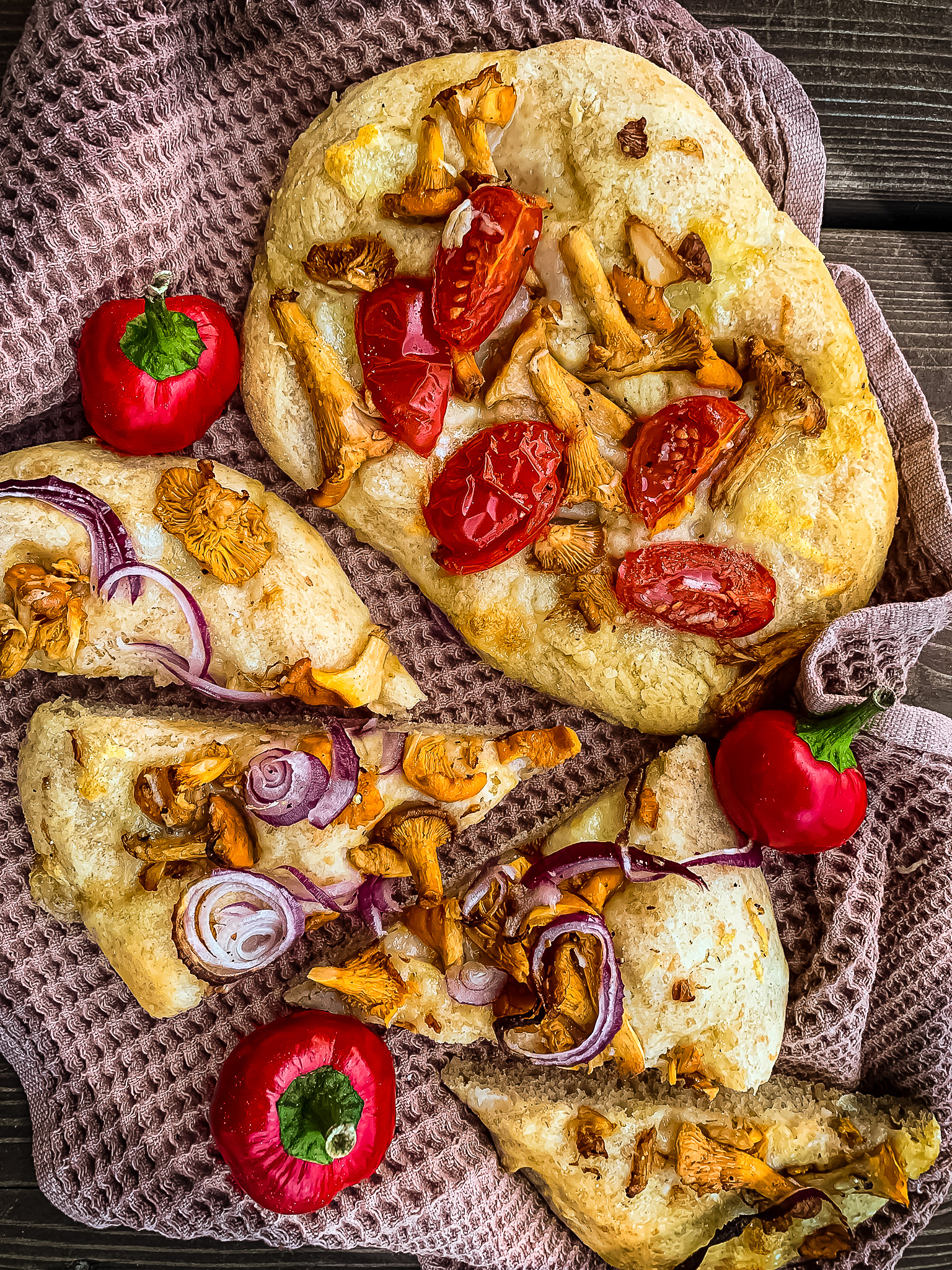 Foccacia with tomatoes, mushrooms, onion and bell peppers on a textured brown towel