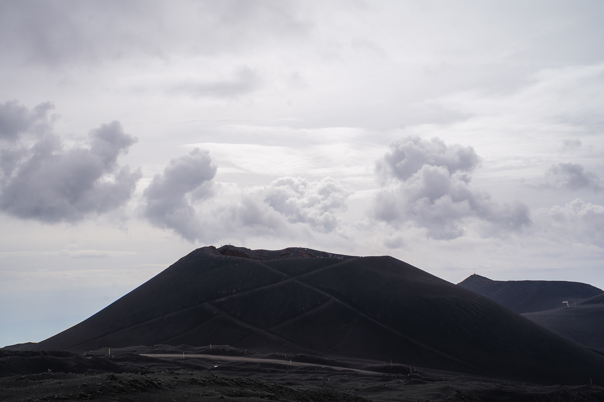 Paysage désertique des cratères latéraux de l'Etna sous un ciel chargé de nuages, illustrant la puissance de la géologie volcanique en Sicile.