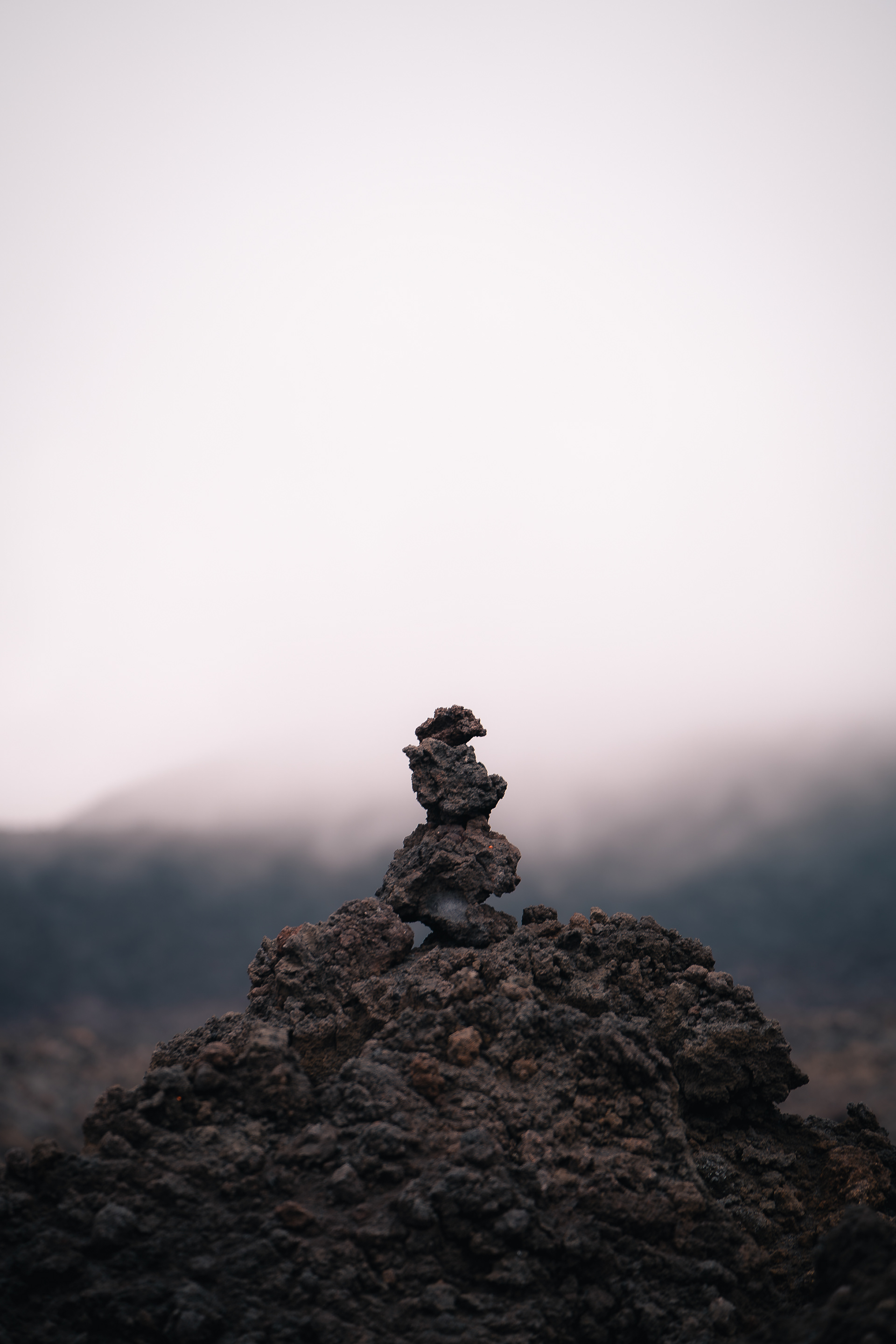 Détail d'un cairn (empilement de pierres) en roche de lave sur fond de paysage volcanique brumeux et atmosphérique.