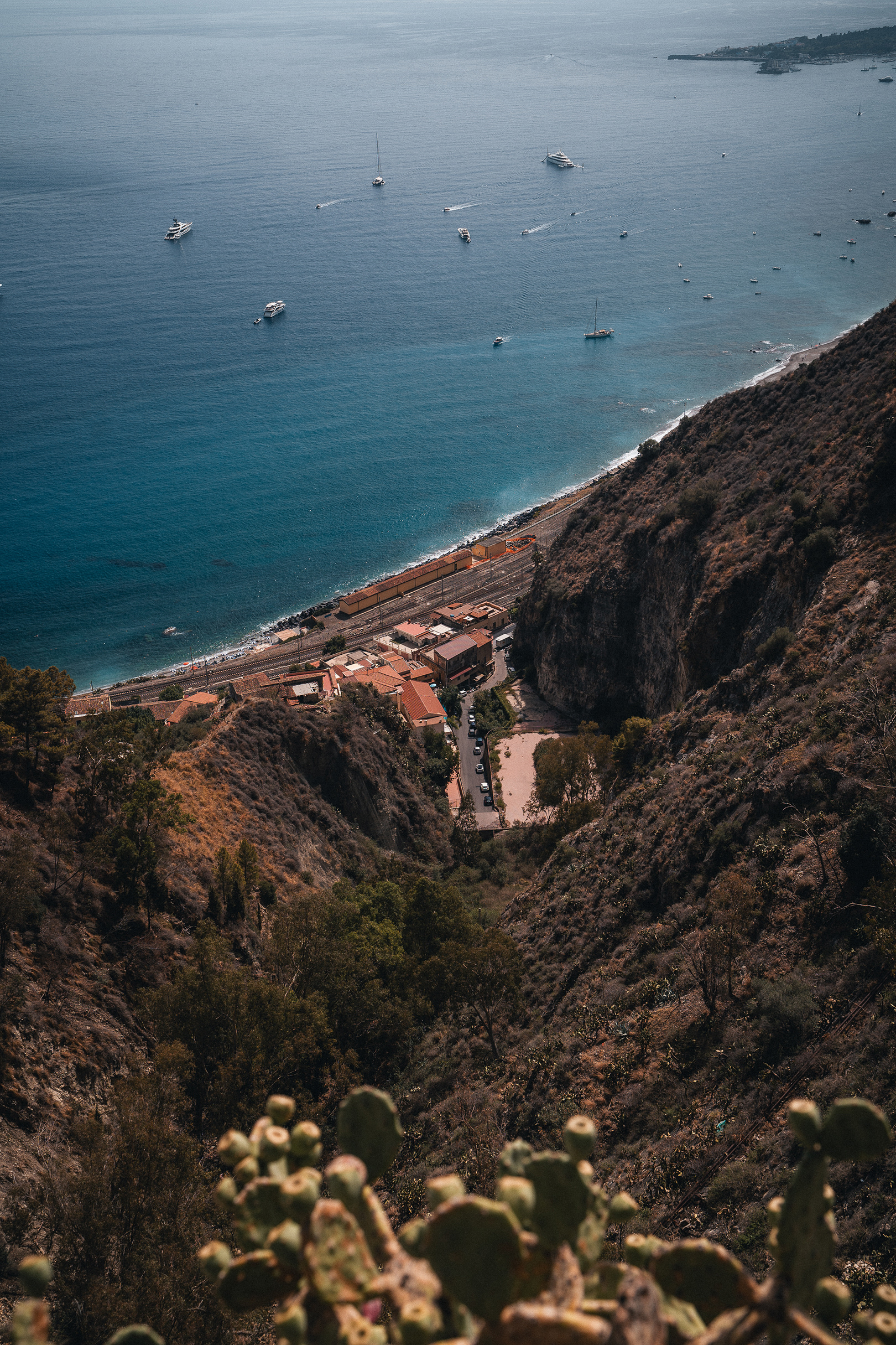 Vue plongeante sur les eaux turquoise de la Sicile et les bateaux au large de Taormine, par Sabri Kaced.