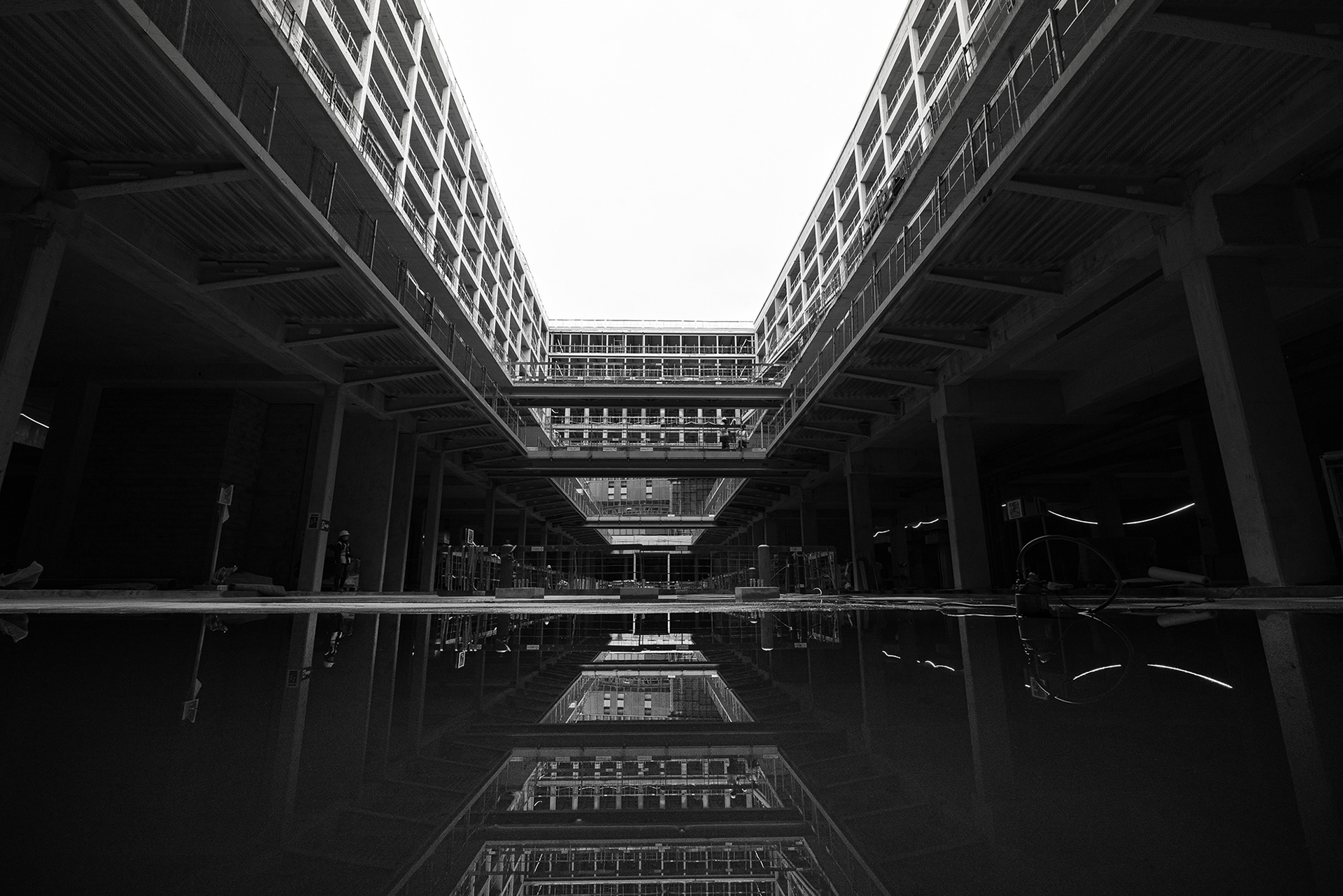Photo d'architecture symétrique en noir et blanc du patio intérieur d'un immeuble en construction à Paris Austerlitz, reflet dans une flaque d'eau par Sabri Kaced.