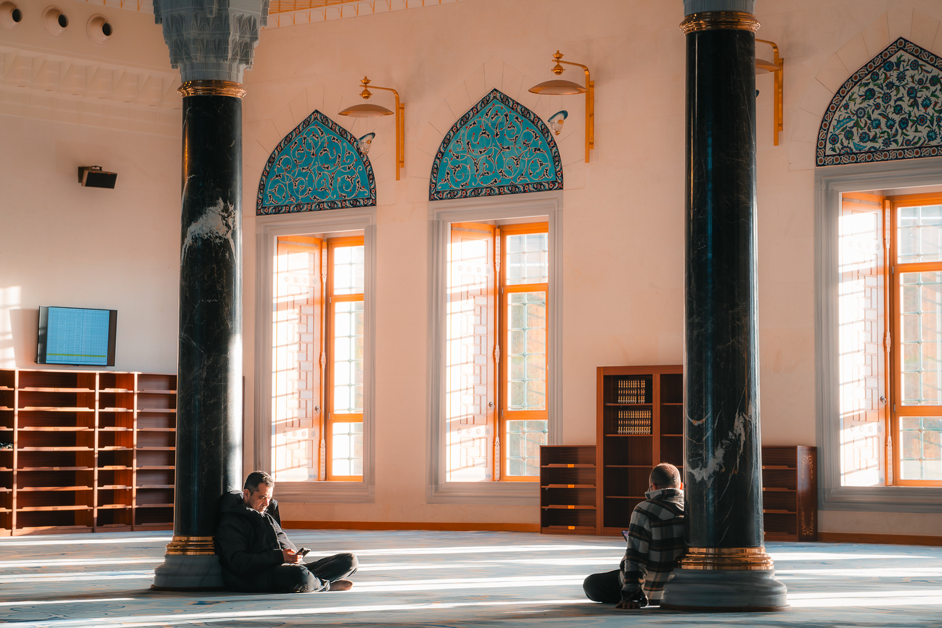 Scène de vie intérieure dans une mosquée photographiée par Sabri Kaced, mettant en avant des colonnes en marbre noir et la lumière naturelle filtrant à travers de grandes fenêtres.