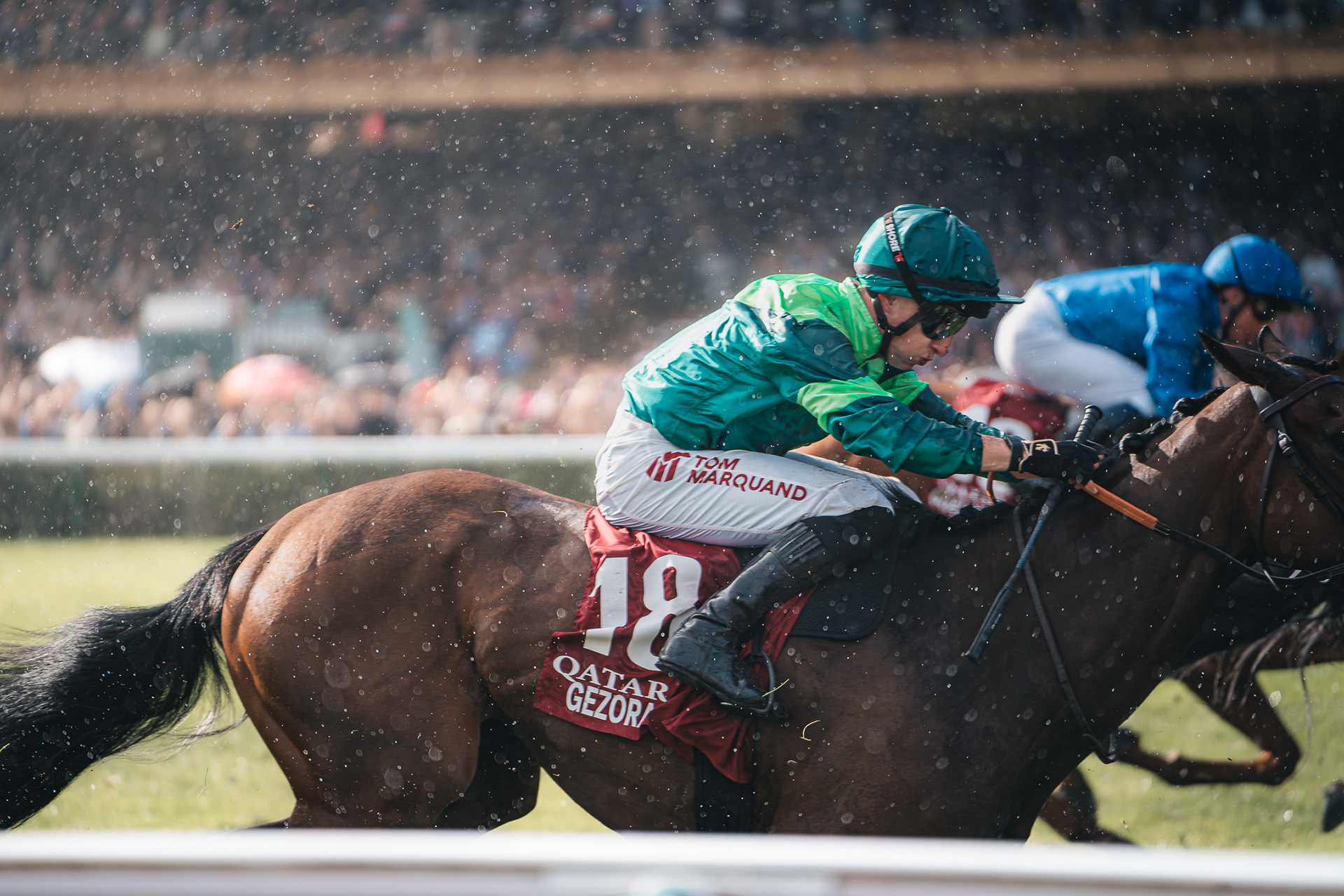 Photo de Sabri Kaced montrant le jockey Tom Marquand en plein effort, penché sur son cheval au galop sous une légère pluie ou projection d'eau.