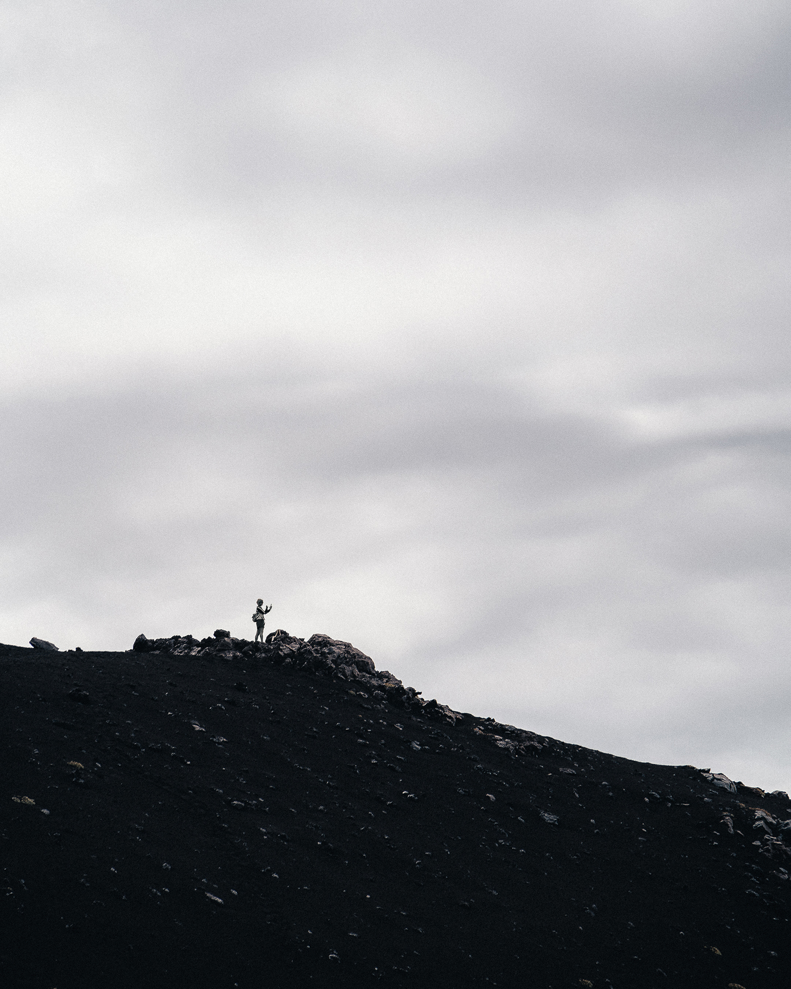 Silhouette d'un photographe seul sur une crête volcanique escarpée face à l'immensité d'un ciel nuageux, style photographie documentaire de voyage.