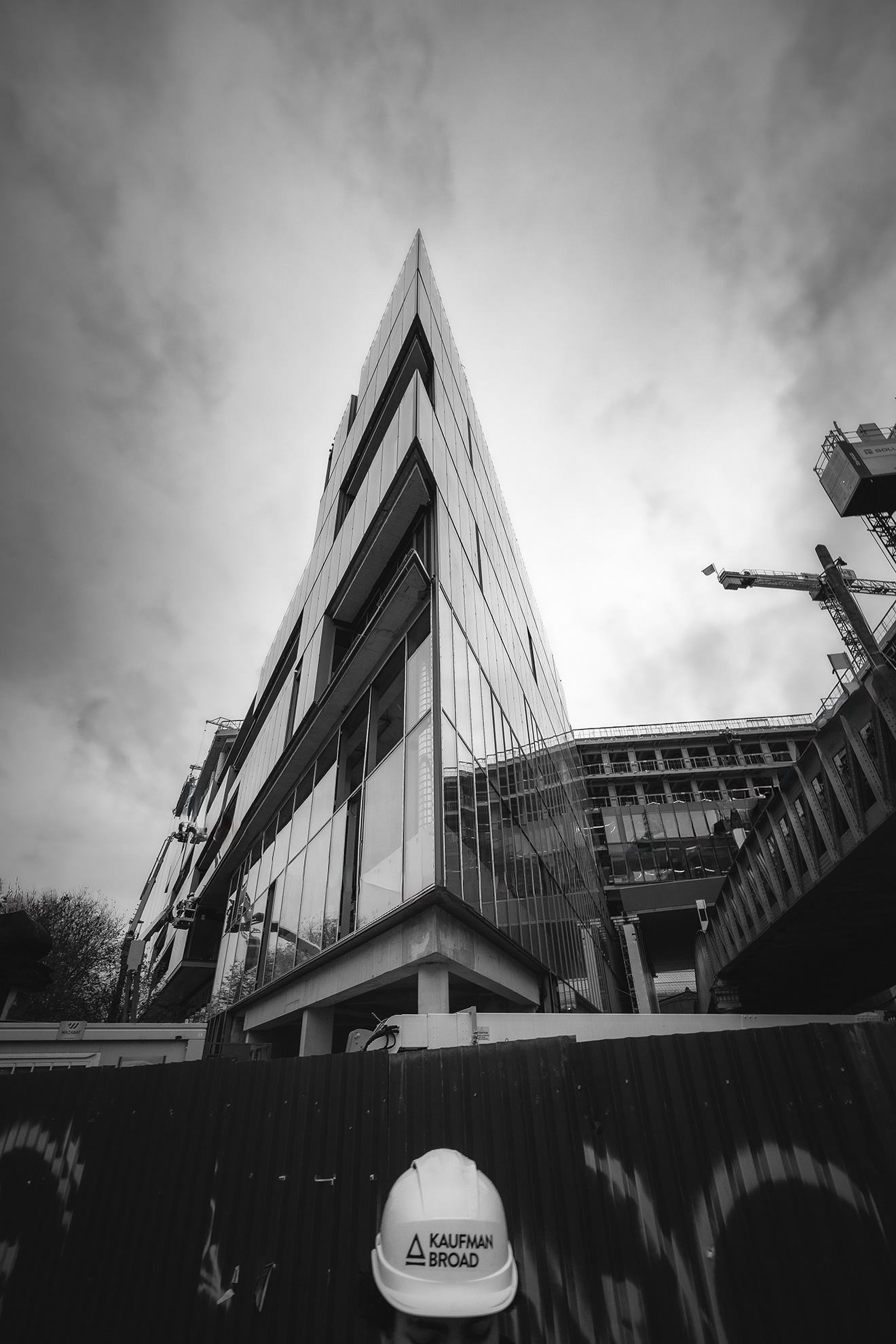 Façade en verre de l'immeuble Kaufman & Broad à Austerlitz avec casque de chantier au premier plan, photographie d'architecture par Sabri Kaced.