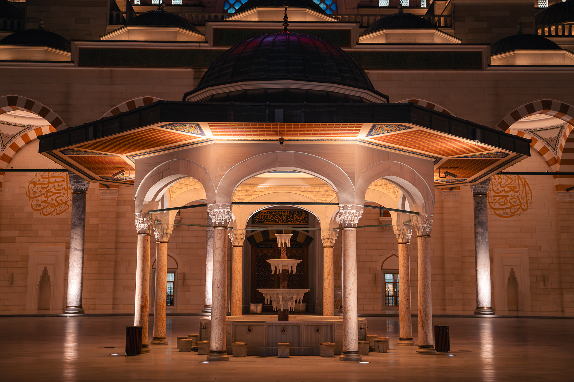 Photographie de Sabri Kaced montrant la fontaine d'ablutions sous un dôme illuminé dans la cour intérieure de la mosquée Camlica à Istanbul, de nuit.